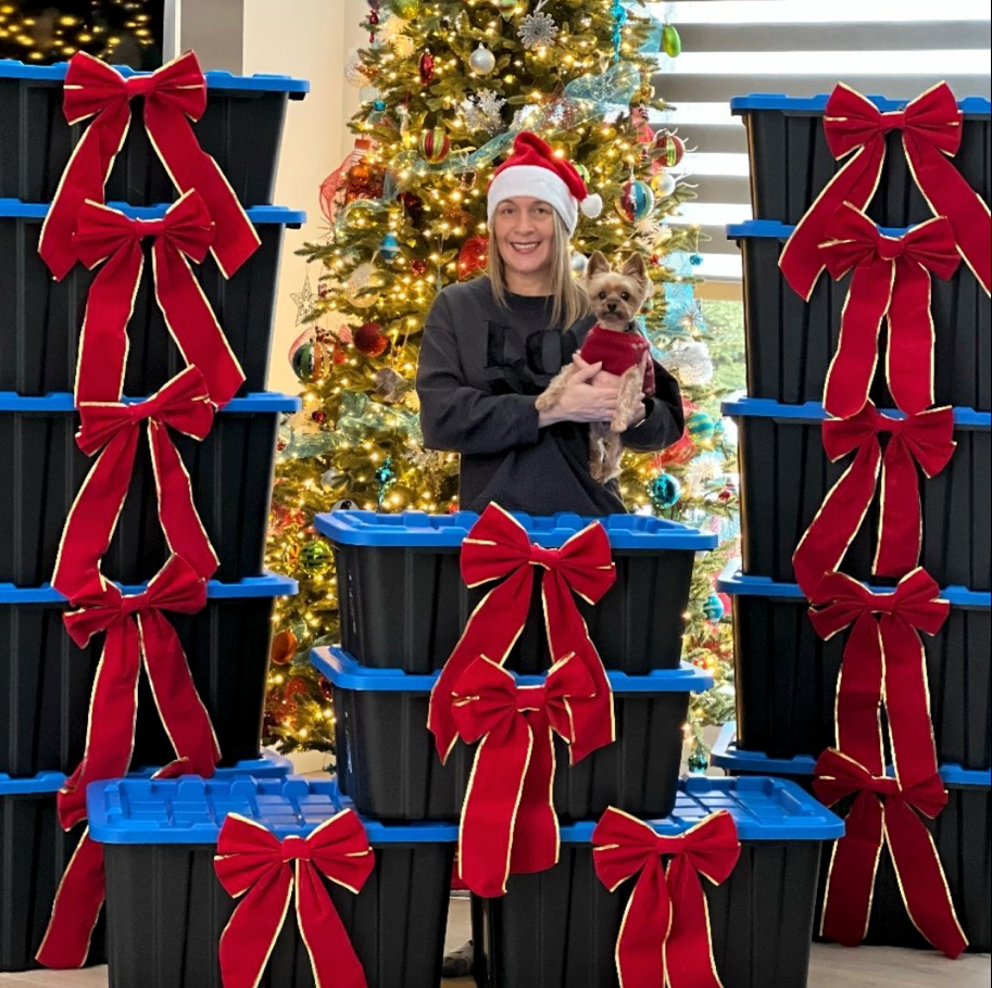A woman in a santa hat is holding a small dog in front of a christmas tree