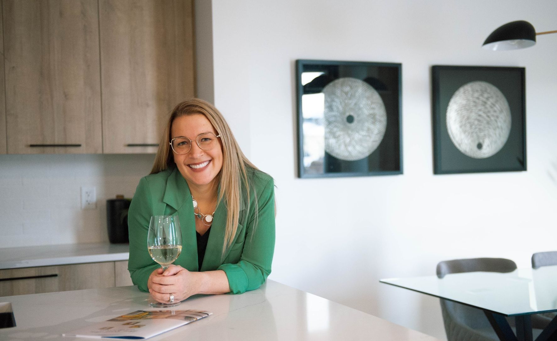 A woman in a green jacket is sitting at a table holding a glass of wine.