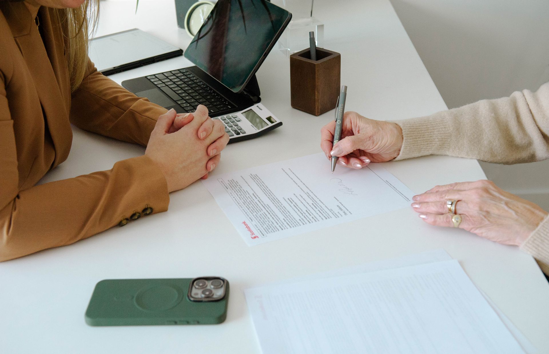 Two women are sitting at a table signing a document.