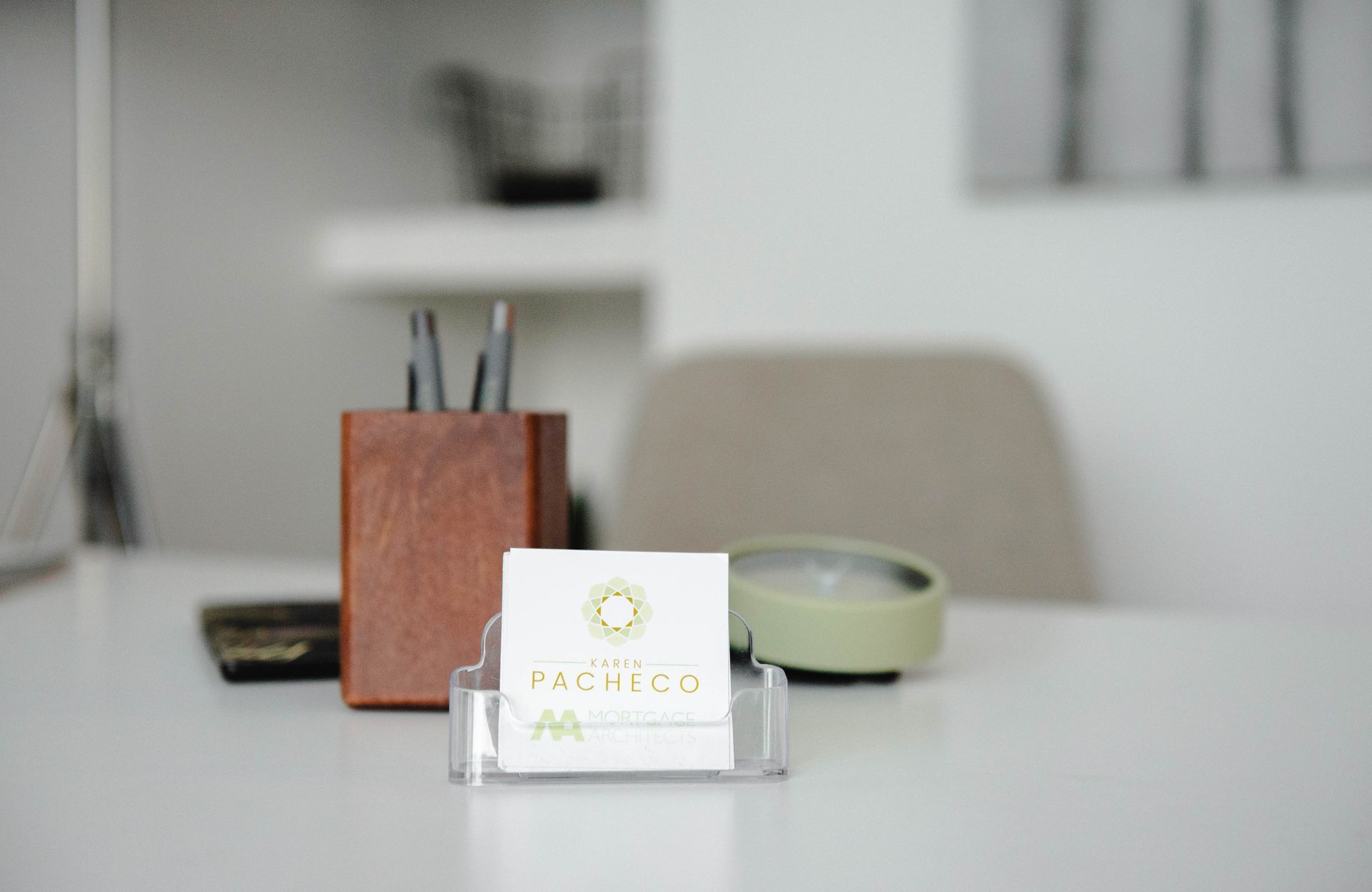A business card is sitting on a desk next to a pen holder.