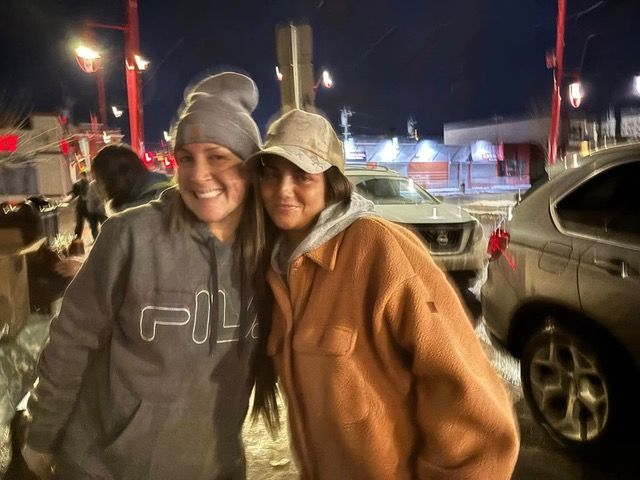 Two women are posing for a picture in a parking lot at night.