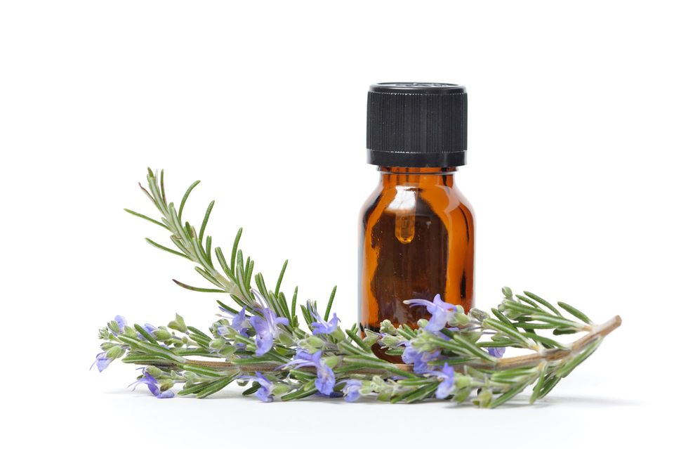 Una bottiglia di olio essenziale di rosmarino con fiori viola su sfondo bianco.