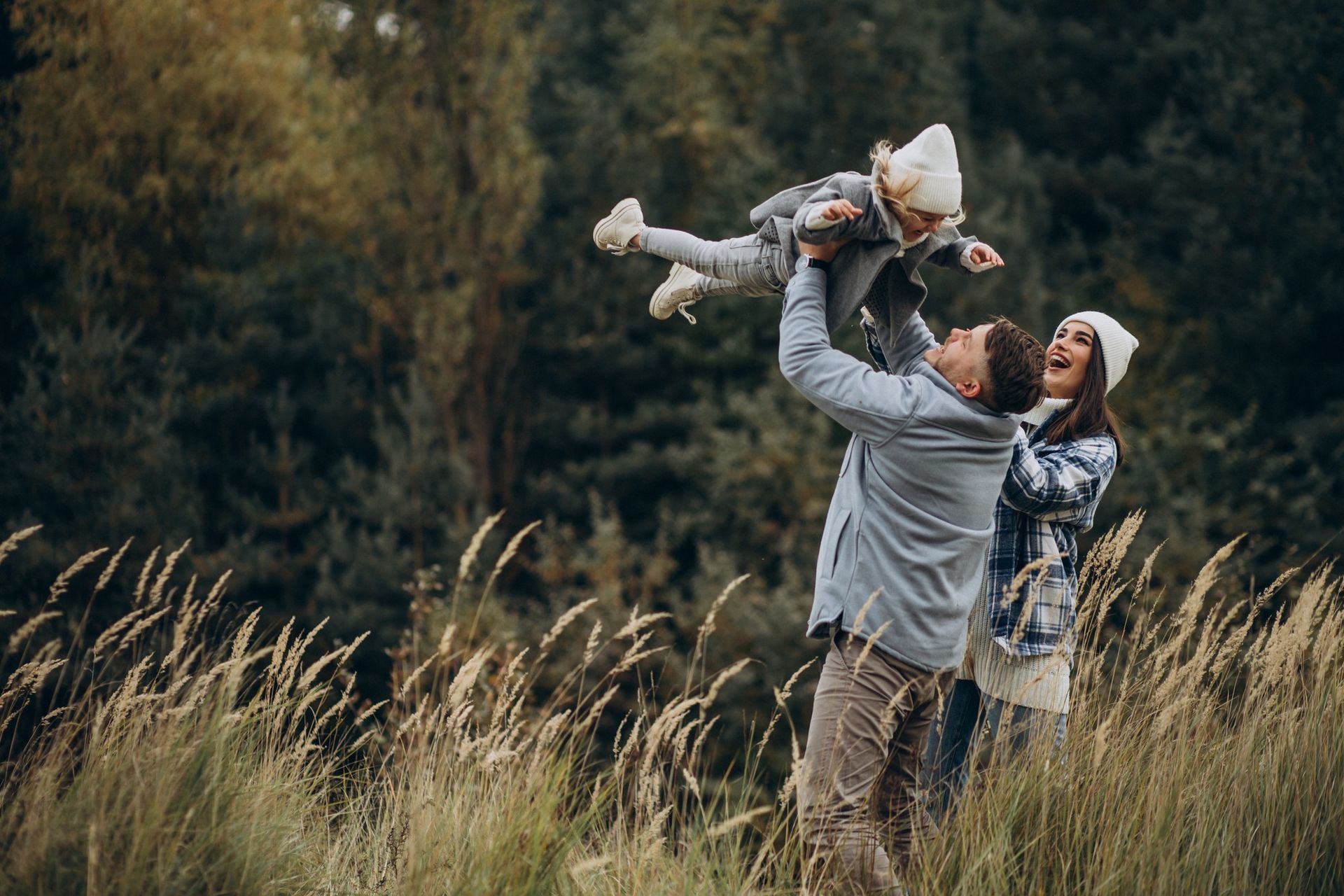 Adult lifting a child overhead in a grassy field, with autumn trees in the background.