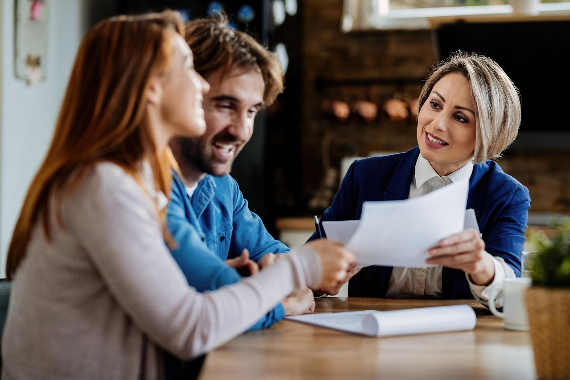 Three people in a meeting, with a woman in blue holding papers and smiling across a table