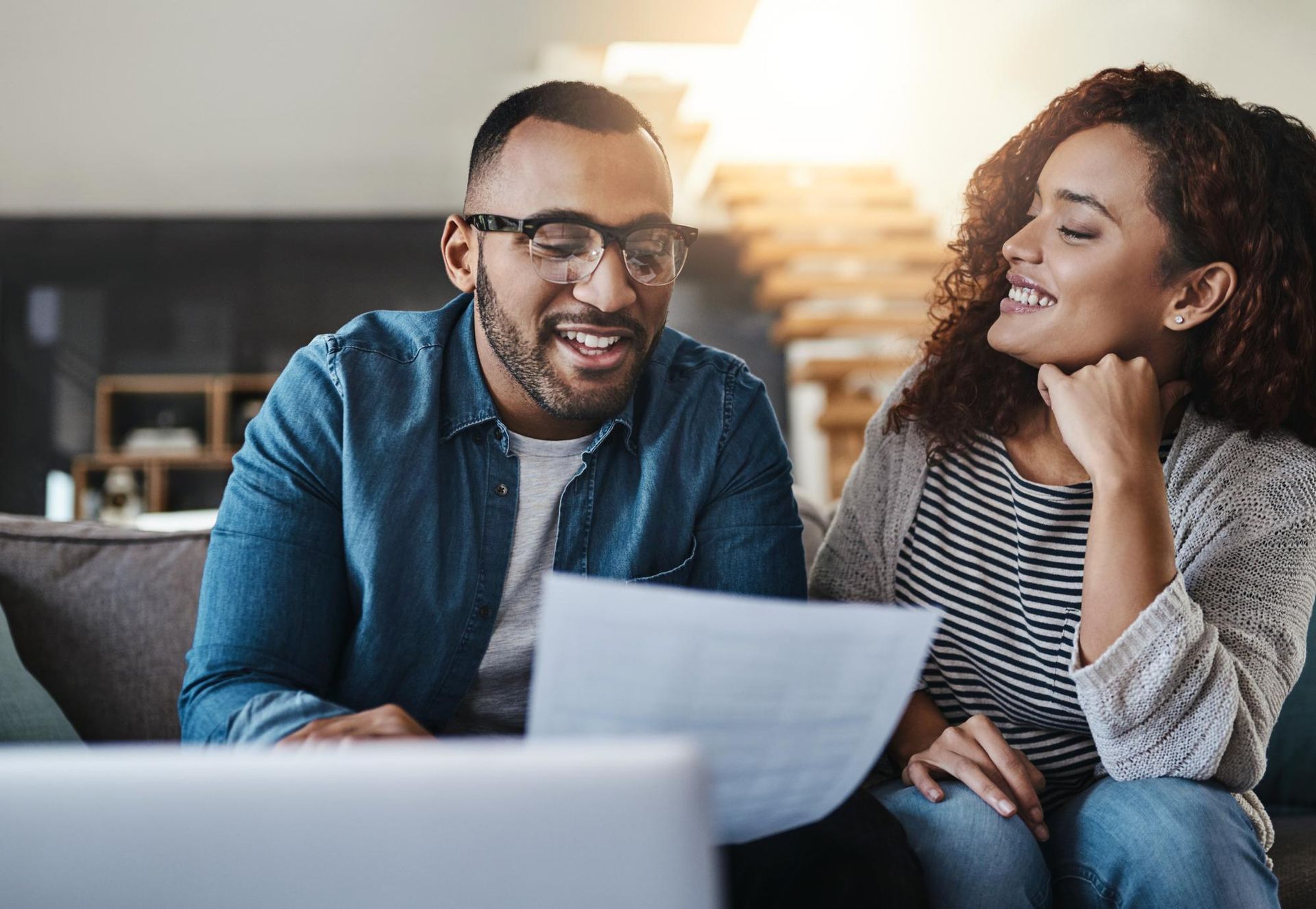 Two coworkers smiling and reviewing a document on a couch in a bright office lounge