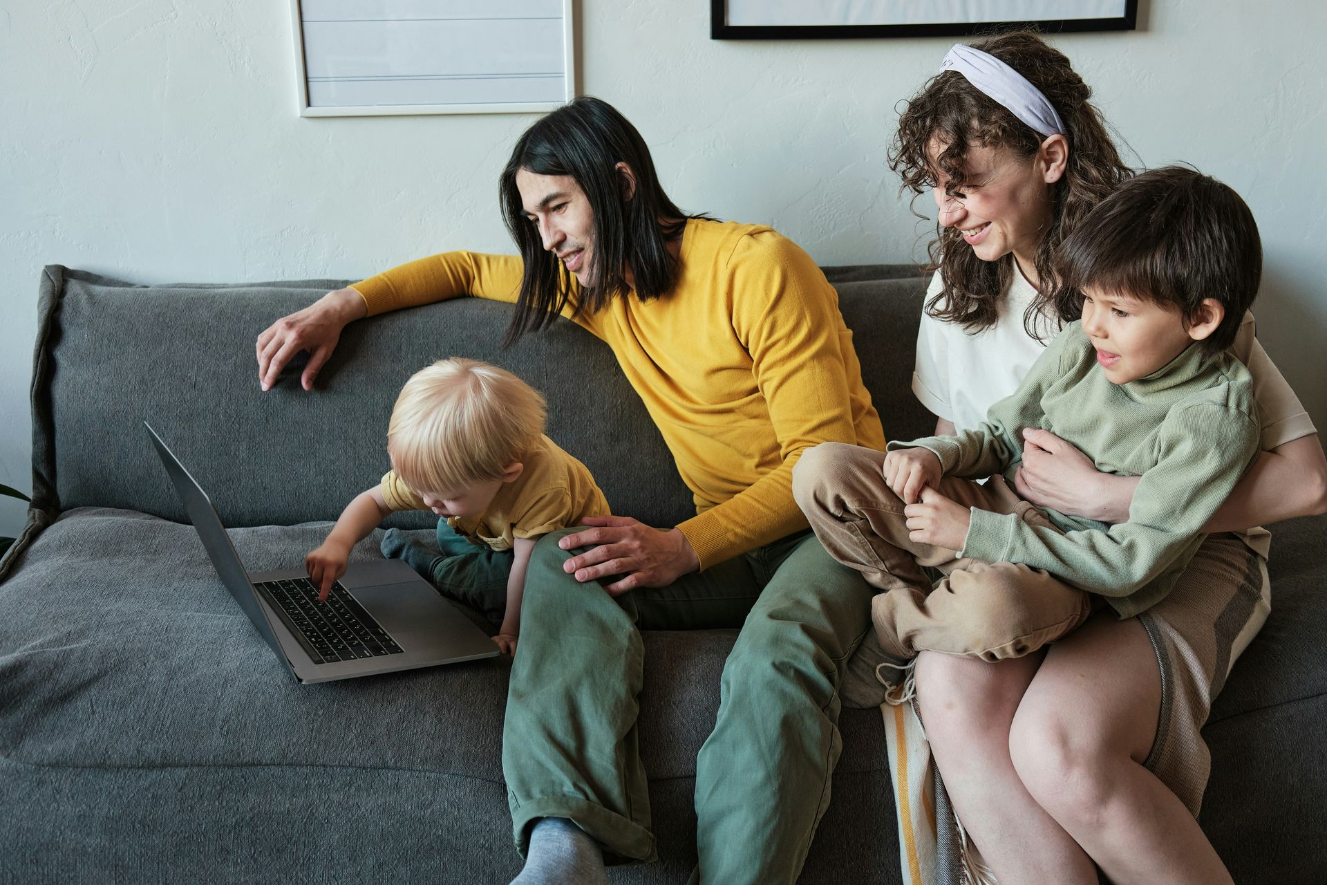 Woman and three children on a gray couch using a laptop together