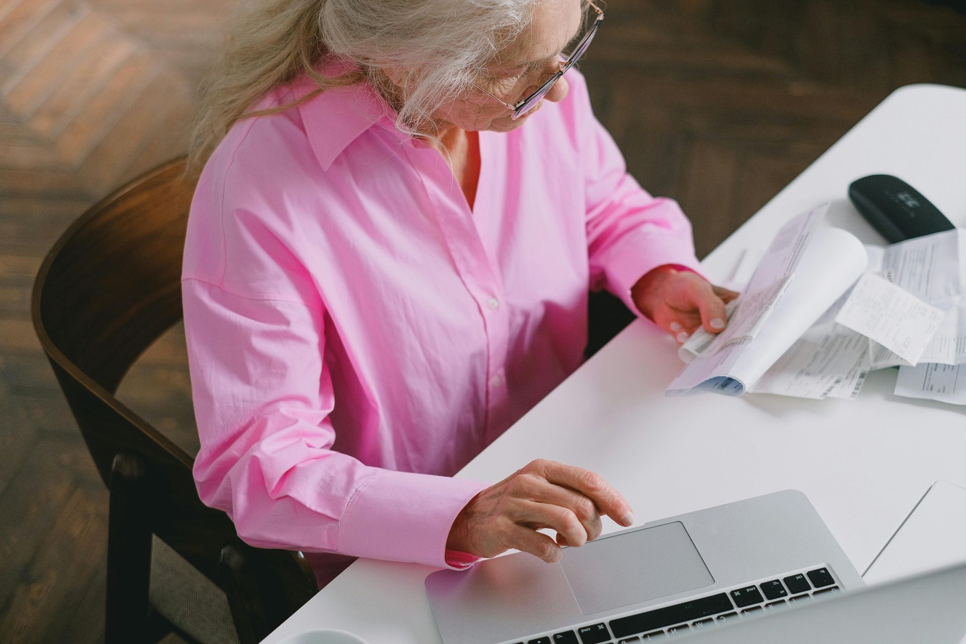 Person in pink shirt reviewing papers at a desk with a laptop and mouse