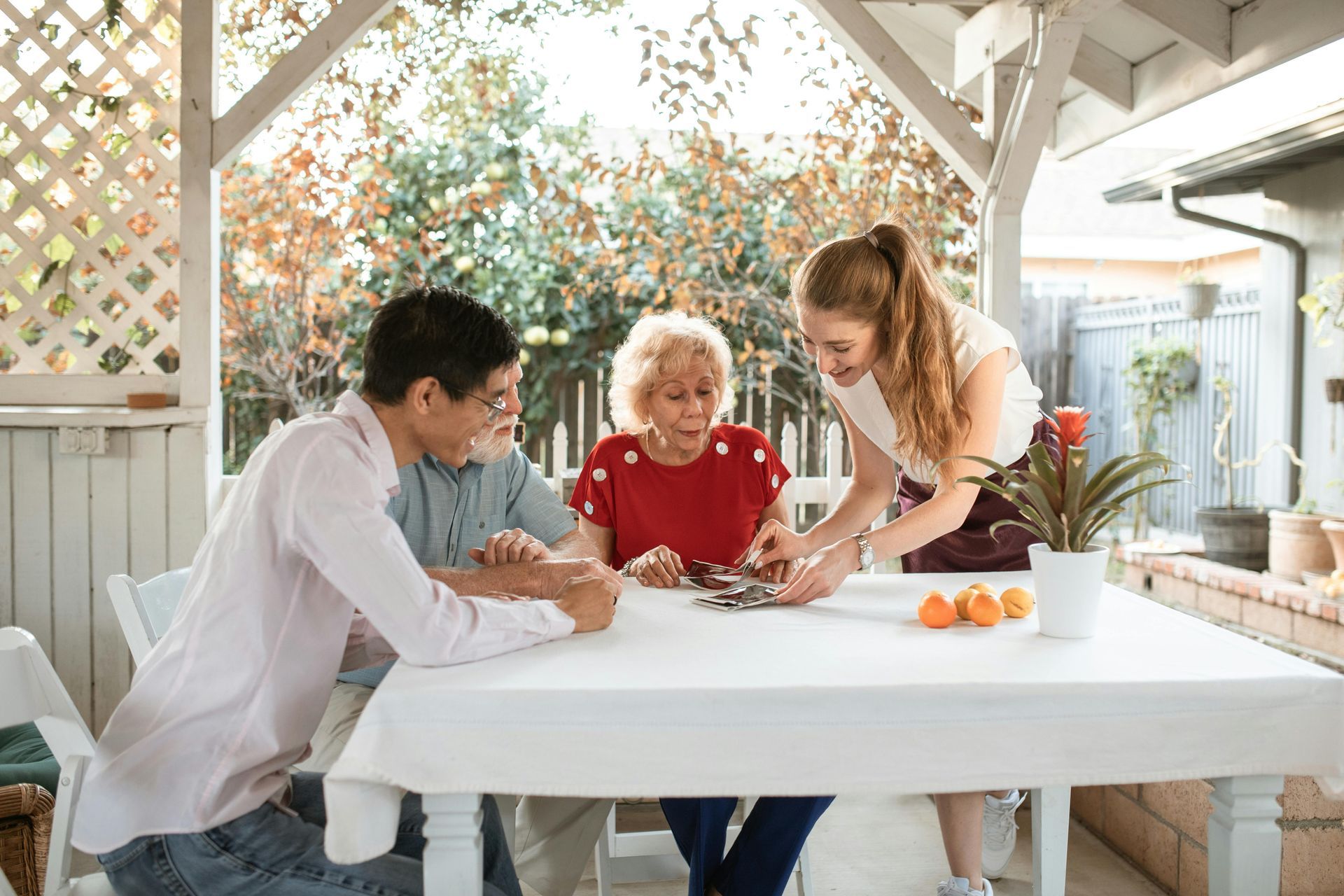 Three people gathered around a white table in a bright patio, writing and discussing over papers and flowers.