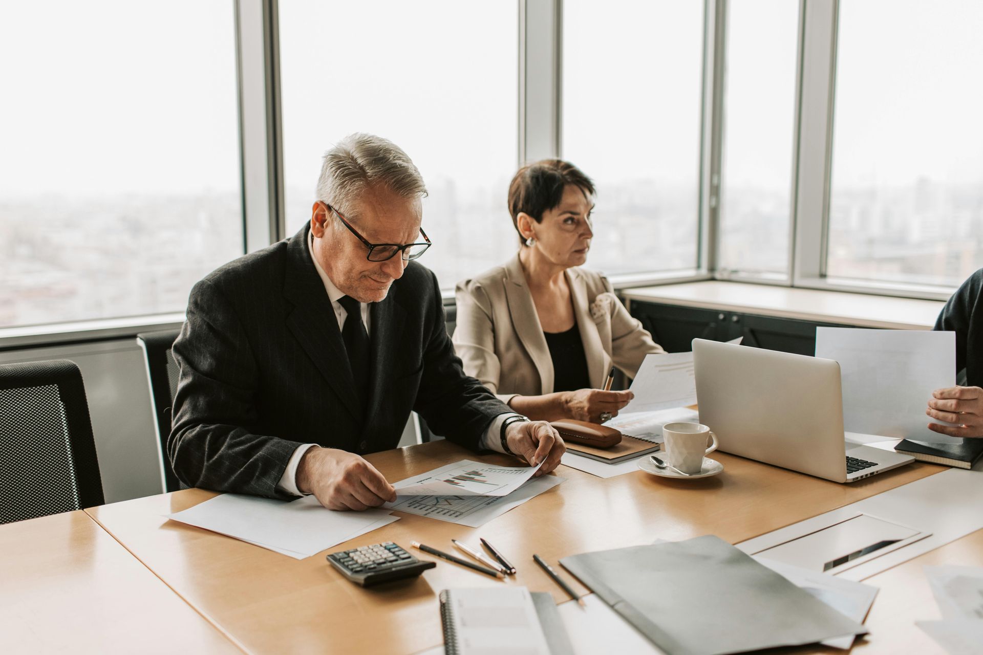 Two people in a bright office meeting, reviewing documents and using a laptop at a conference table