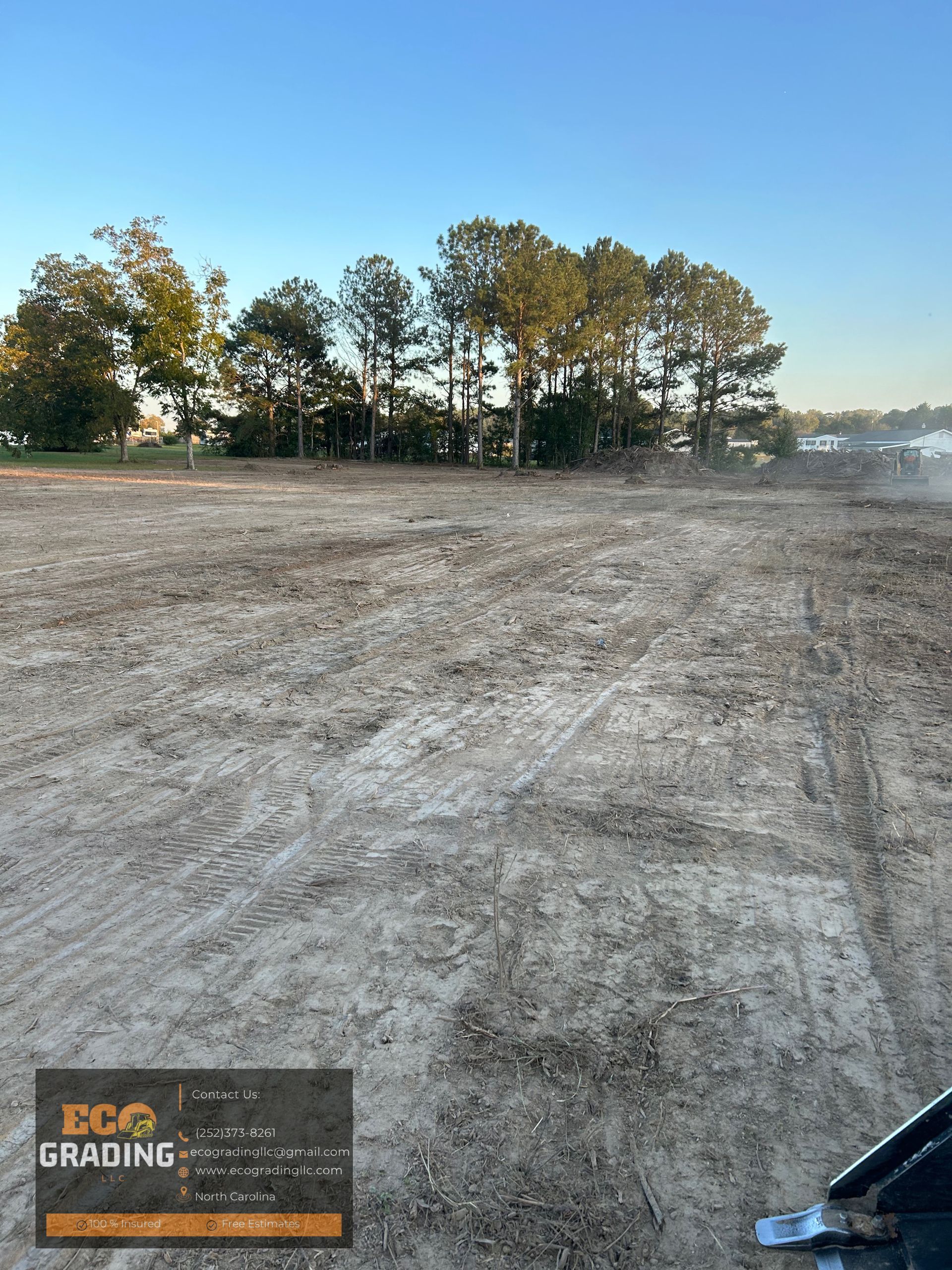 Cleared land, trees in the background, blue sky. Eco Grading logo in the lower left corner.
