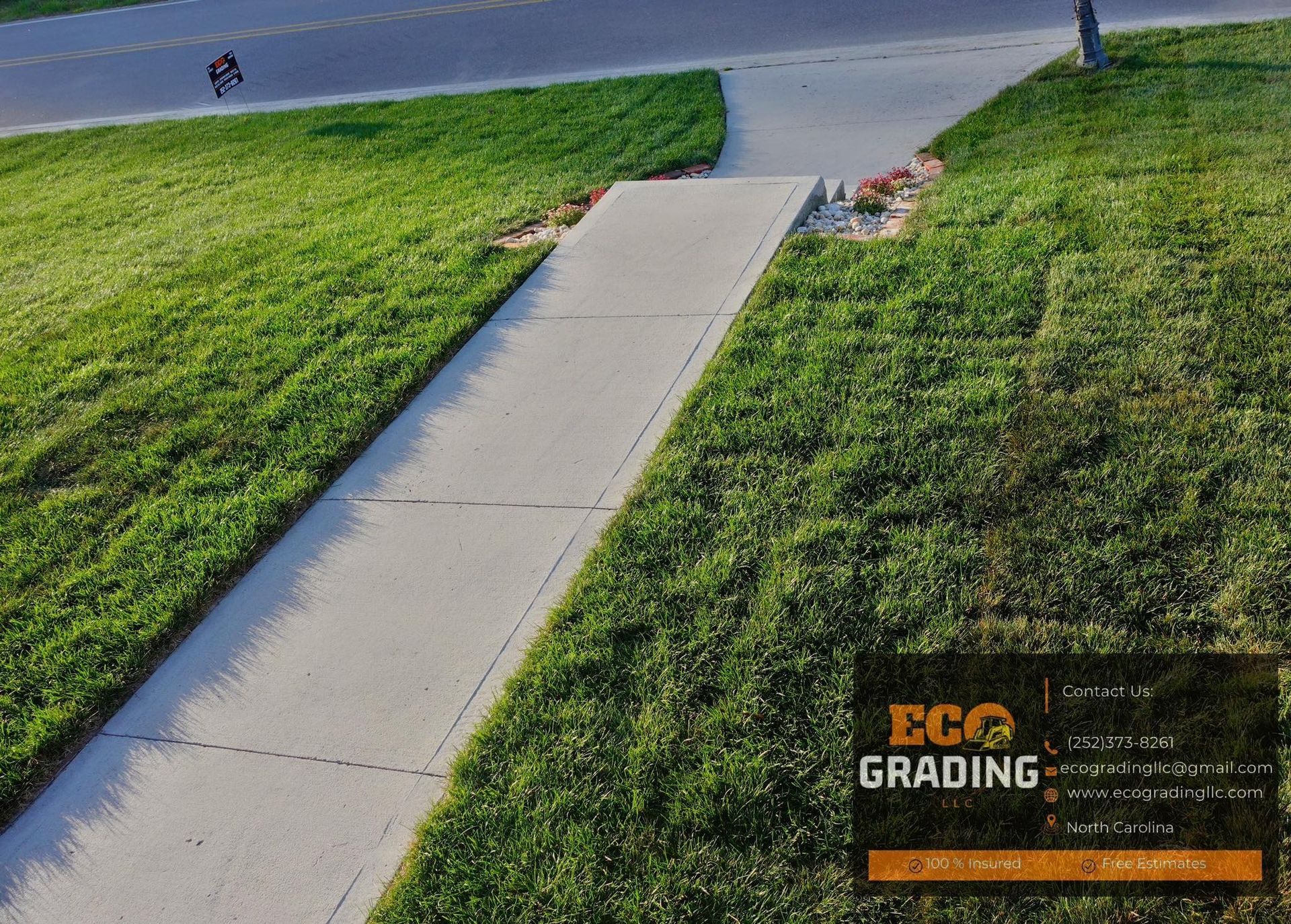 Concrete sidewalk slopes up from lawn to road, with grass and road visible.