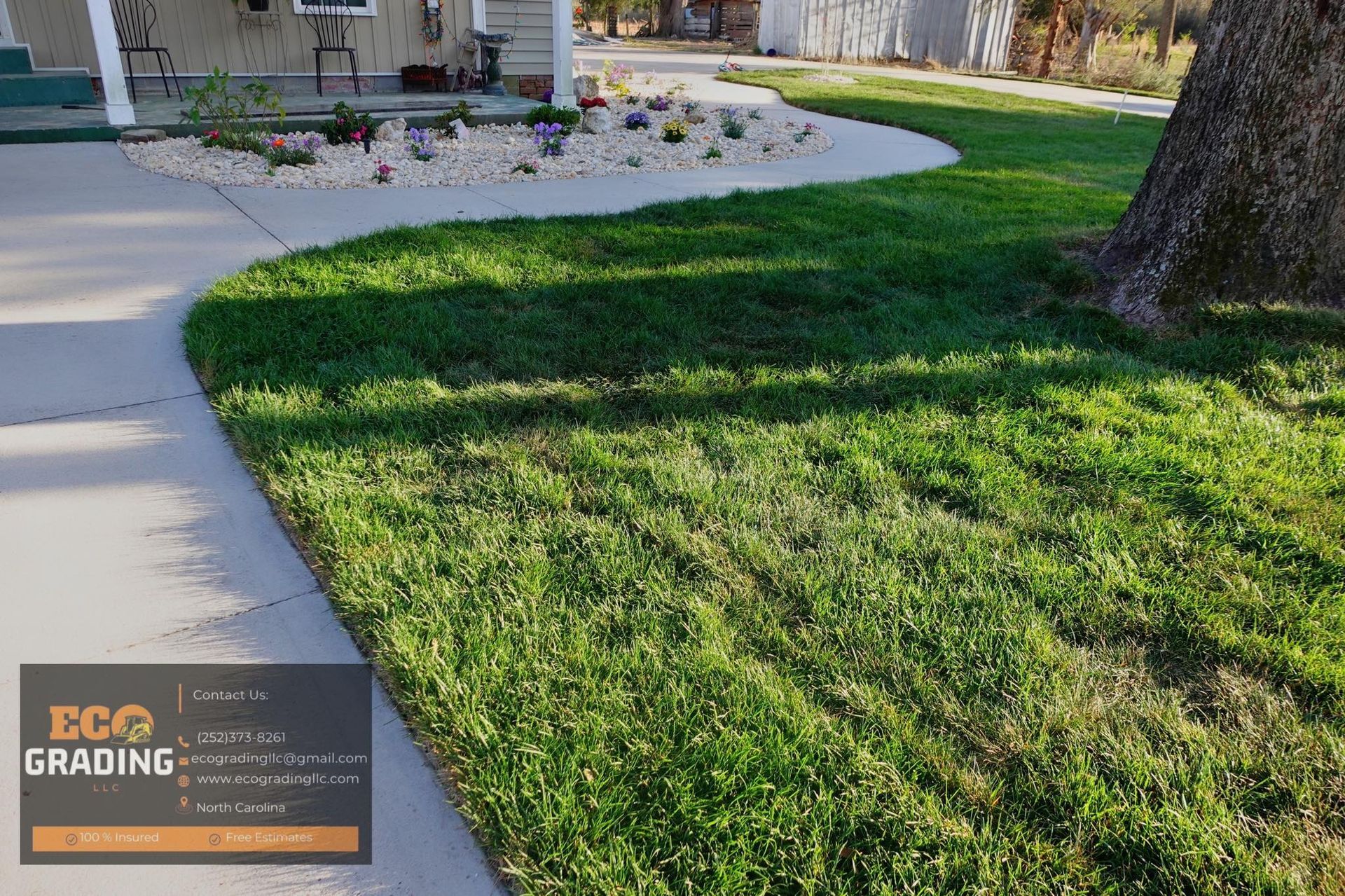 Lawn and curved concrete sidewalk in front of a house, with a flower bed and tree.