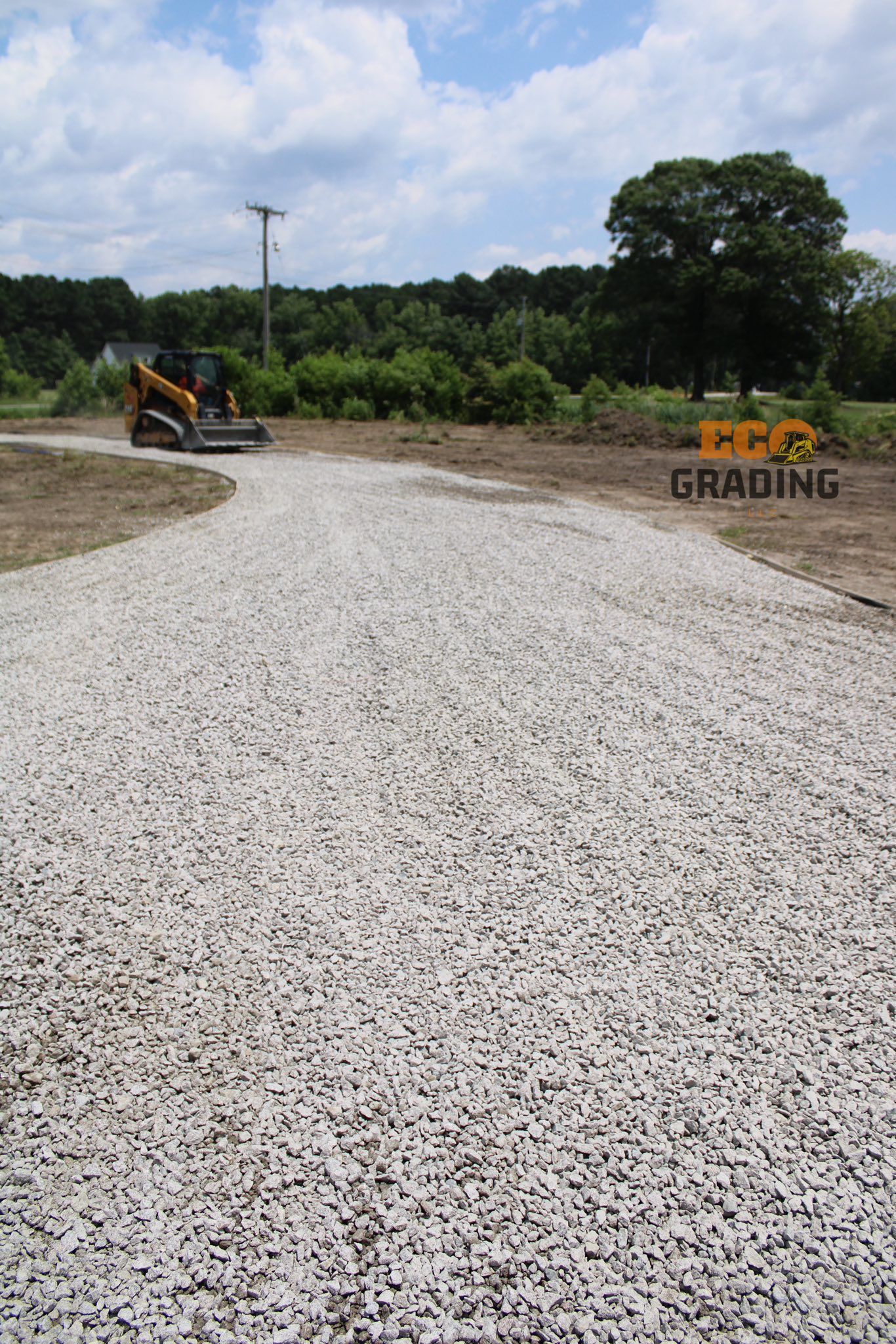 Gravel driveway with a skid steer grading it on a sunny day.
