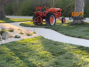 Red tractor parked near a curved sidewalk and tree on a sunny lawn.