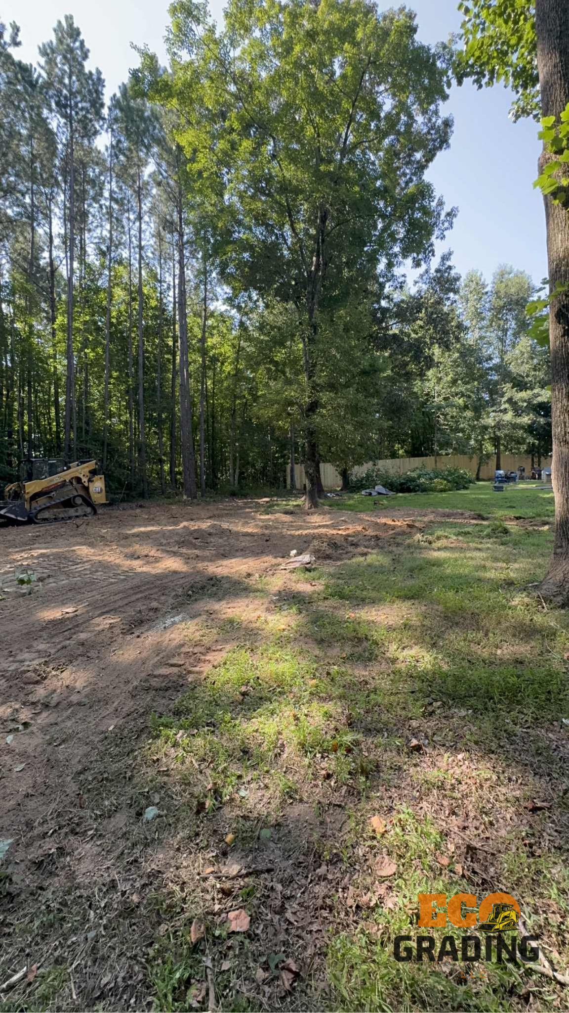 Cleared land, dirt and grass, with trees in background.
