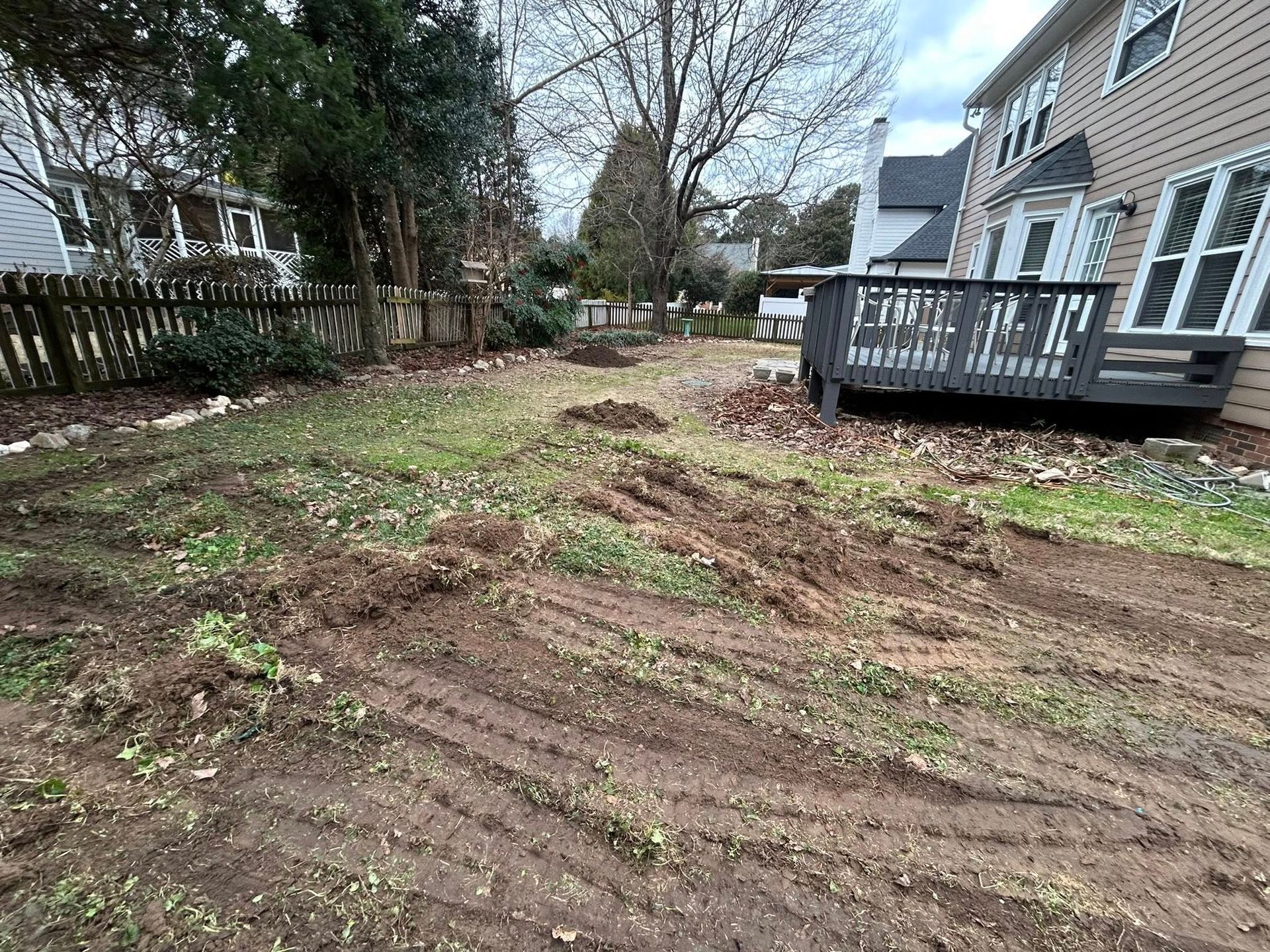 Muddy backyard with tire tracks, small deck, and a wooden fence.