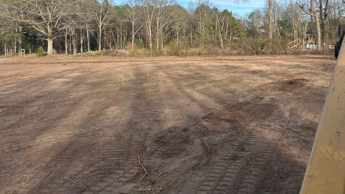Cleared land, brown soil, tire tracks, trees in background, bright day.