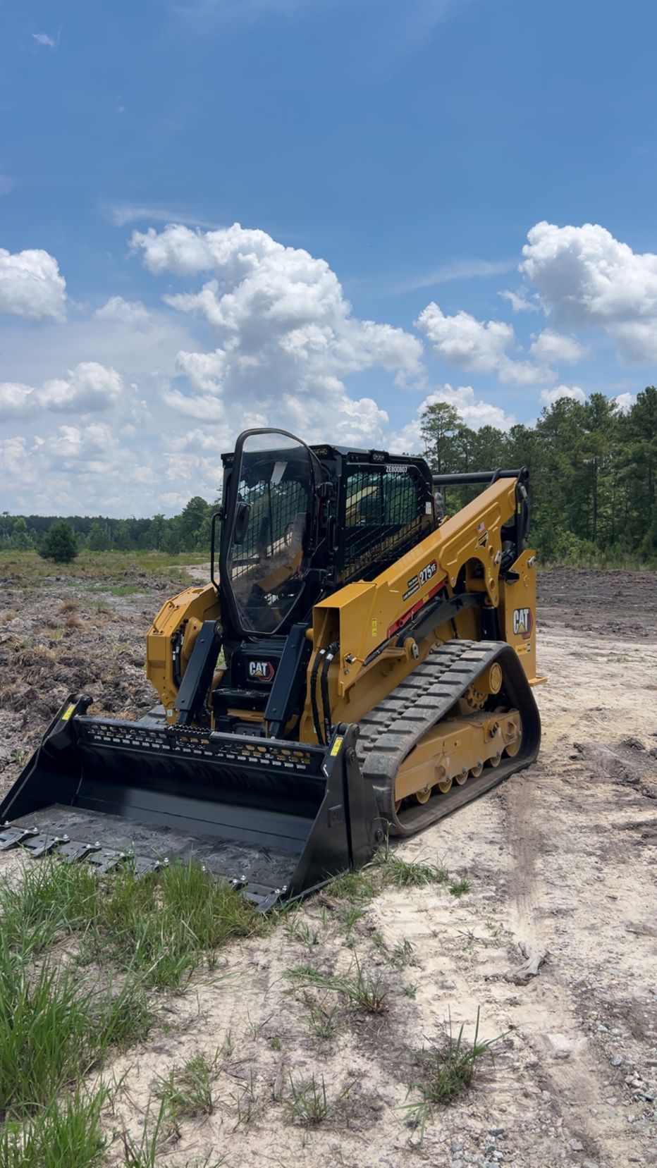 Yellow Caterpillar skid steer loader on tracks, outdoors under blue sky with clouds.