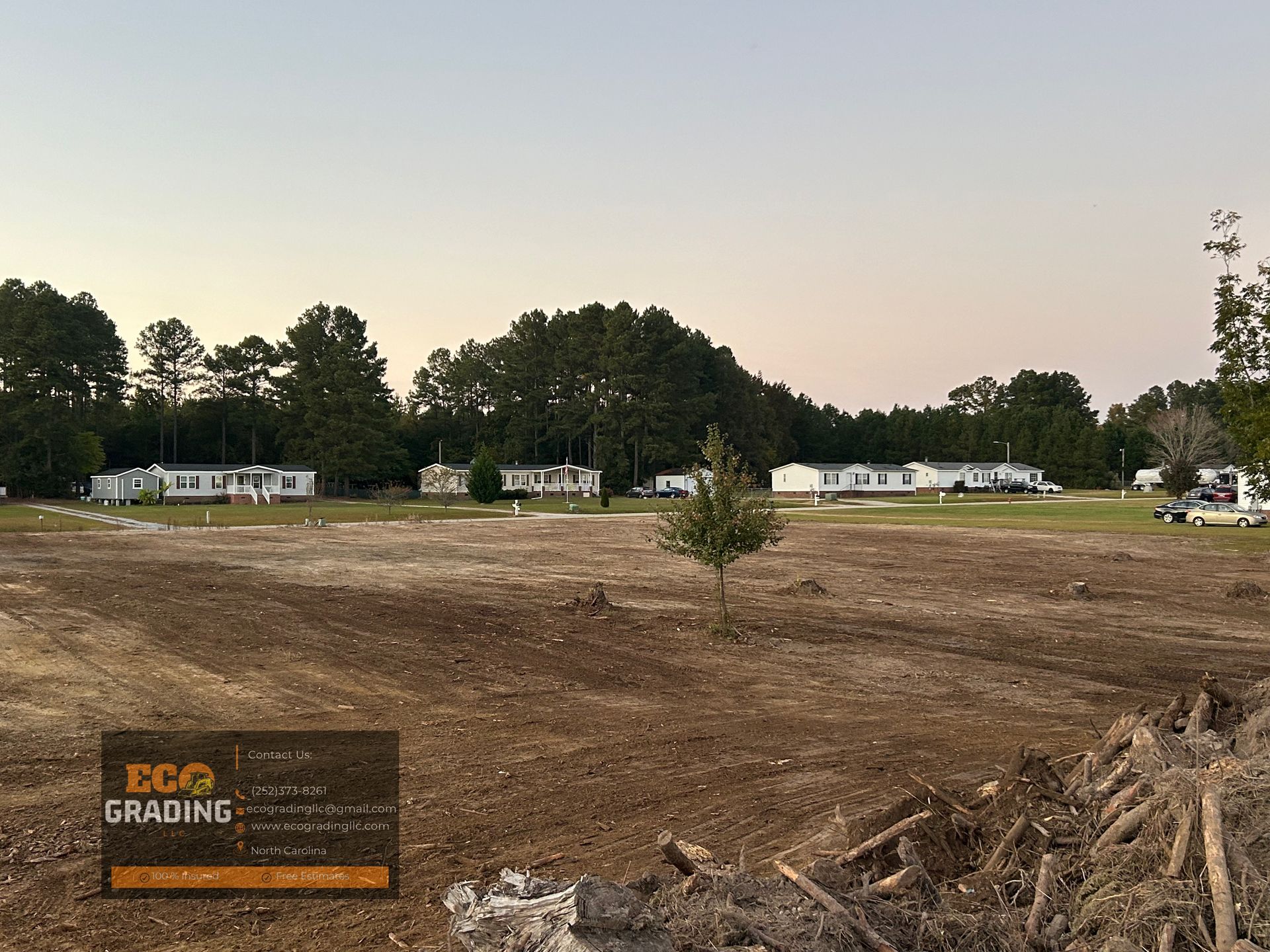 Cleared land with mobile homes in the distance. Dusk sky. 