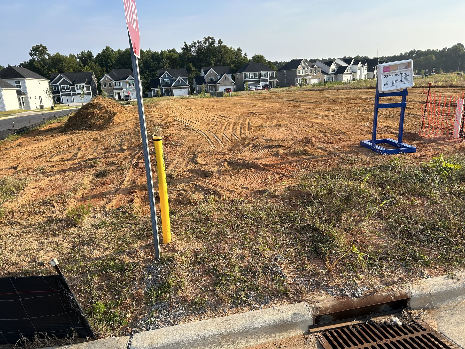 Cleared lot for construction with utility markers and houses in the background.