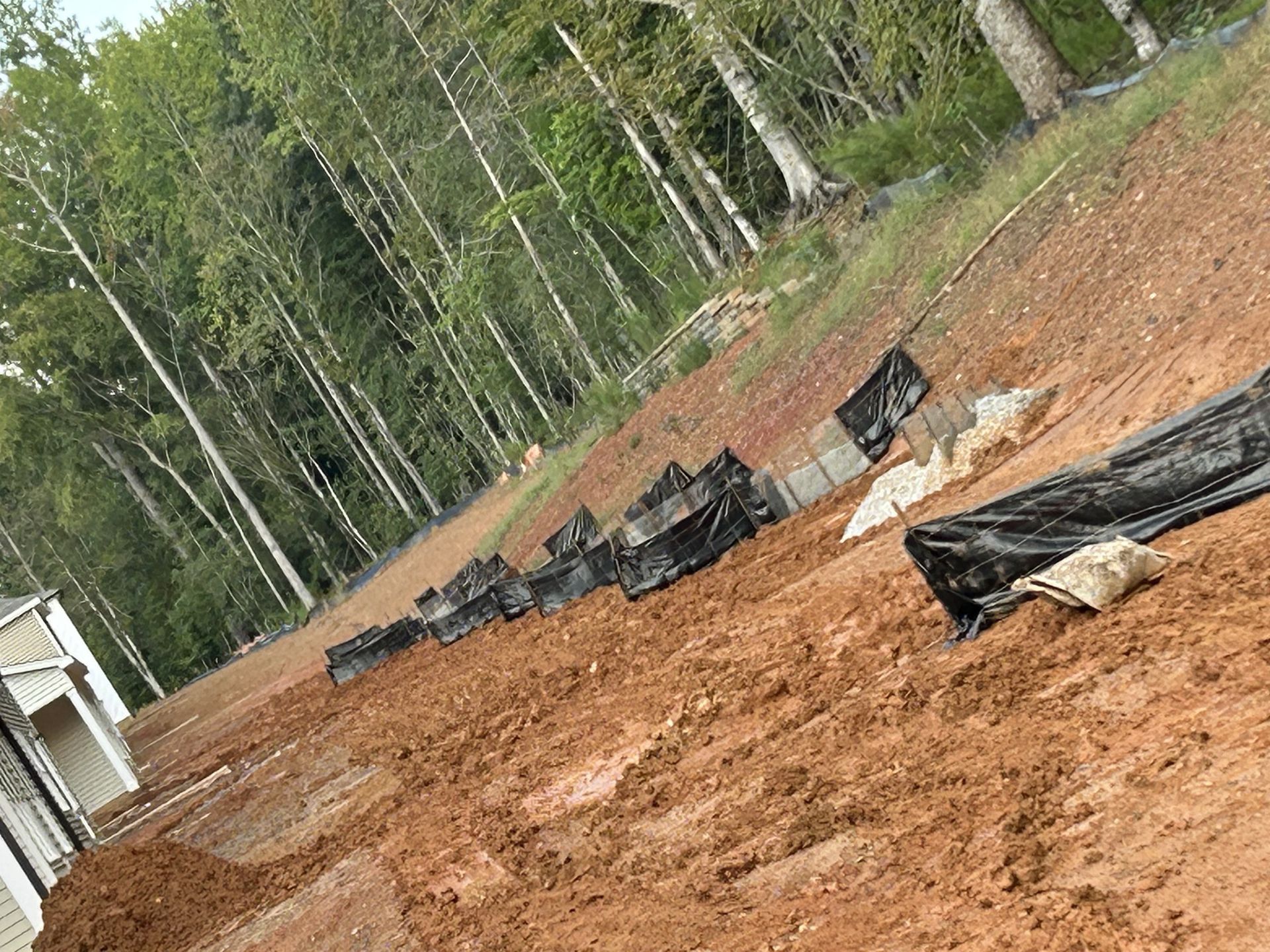 Dirt embankment with black landscaping fabric and some concrete blocks, trees in background.