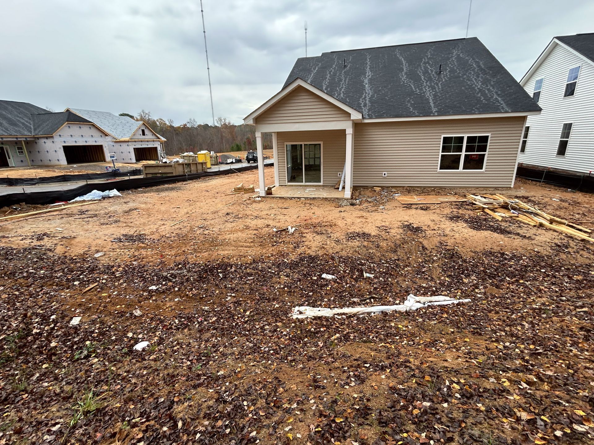 A newly constructed house with tan siding, a dark roof, and a small porch. The yard is bare dirt.