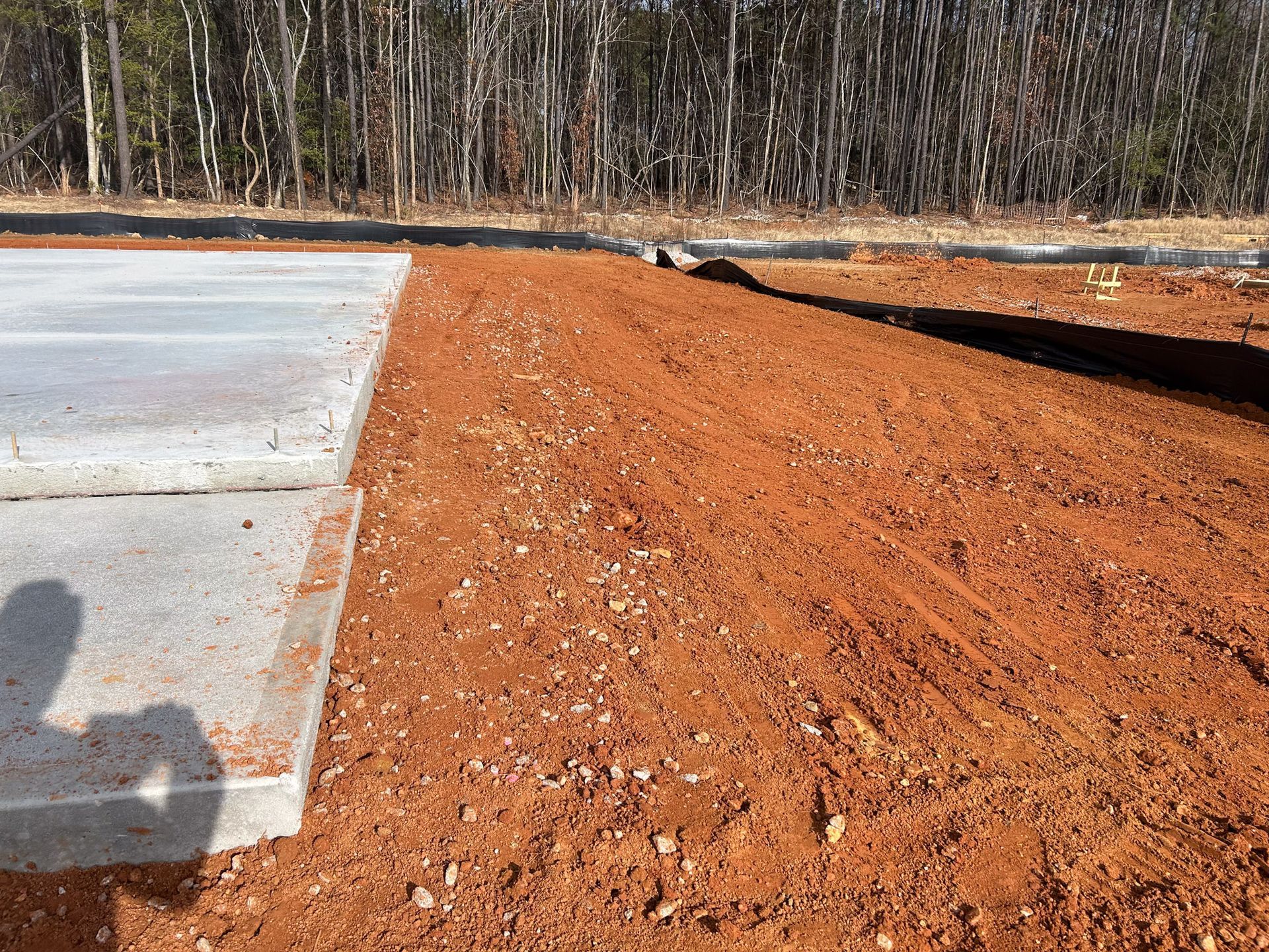 Concrete slab next to red soil, prepared for landscaping, with trees in the background.