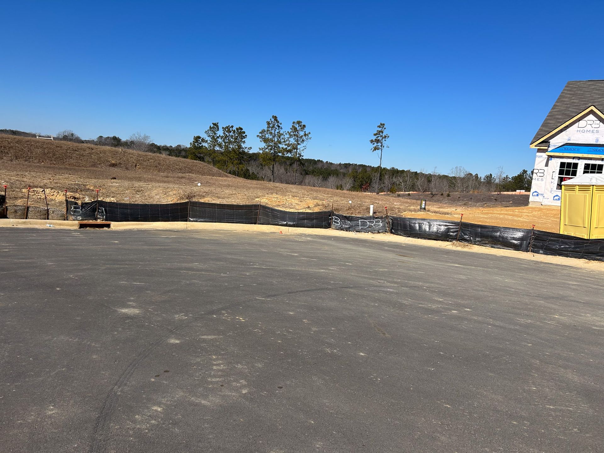 Newly paved asphalt in front of a construction site with a clear blue sky.