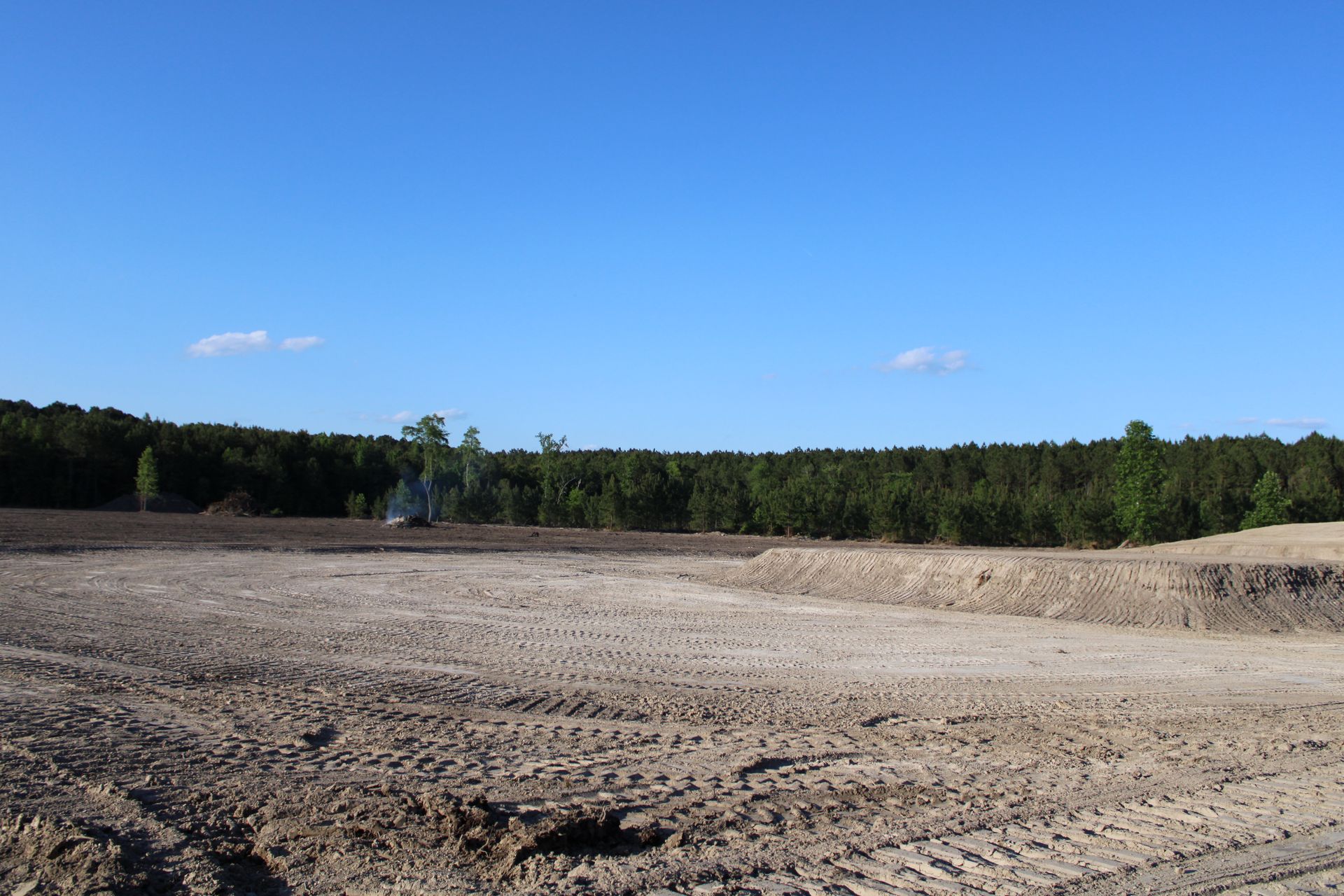 Cleared dirt field bordered by trees under a bright blue sky