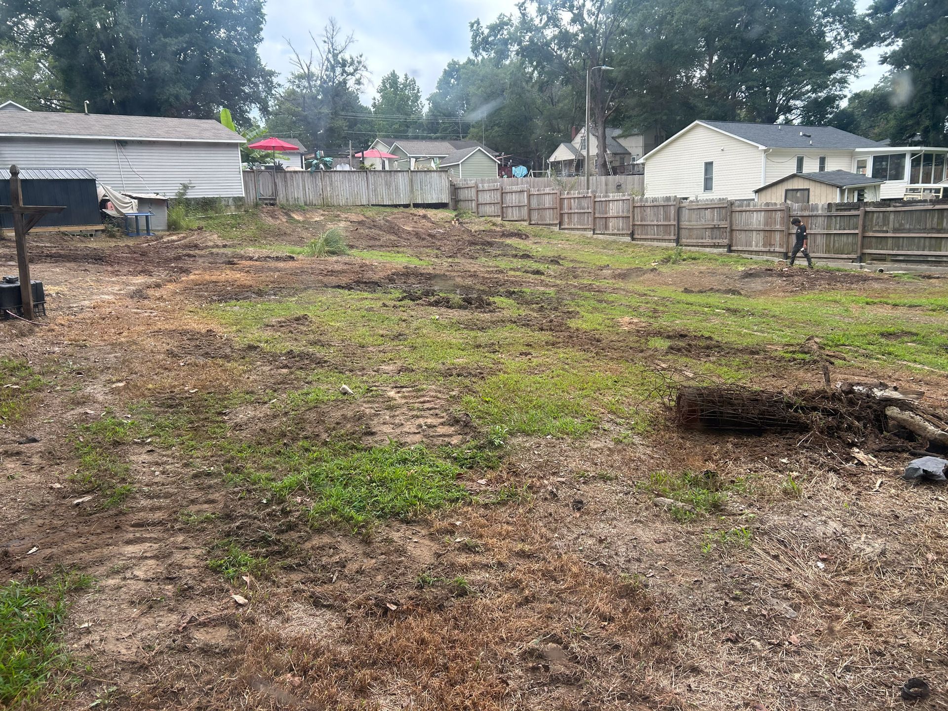 Cleared lot with patchy grass, brown dirt, and wooden fence in a residential area.