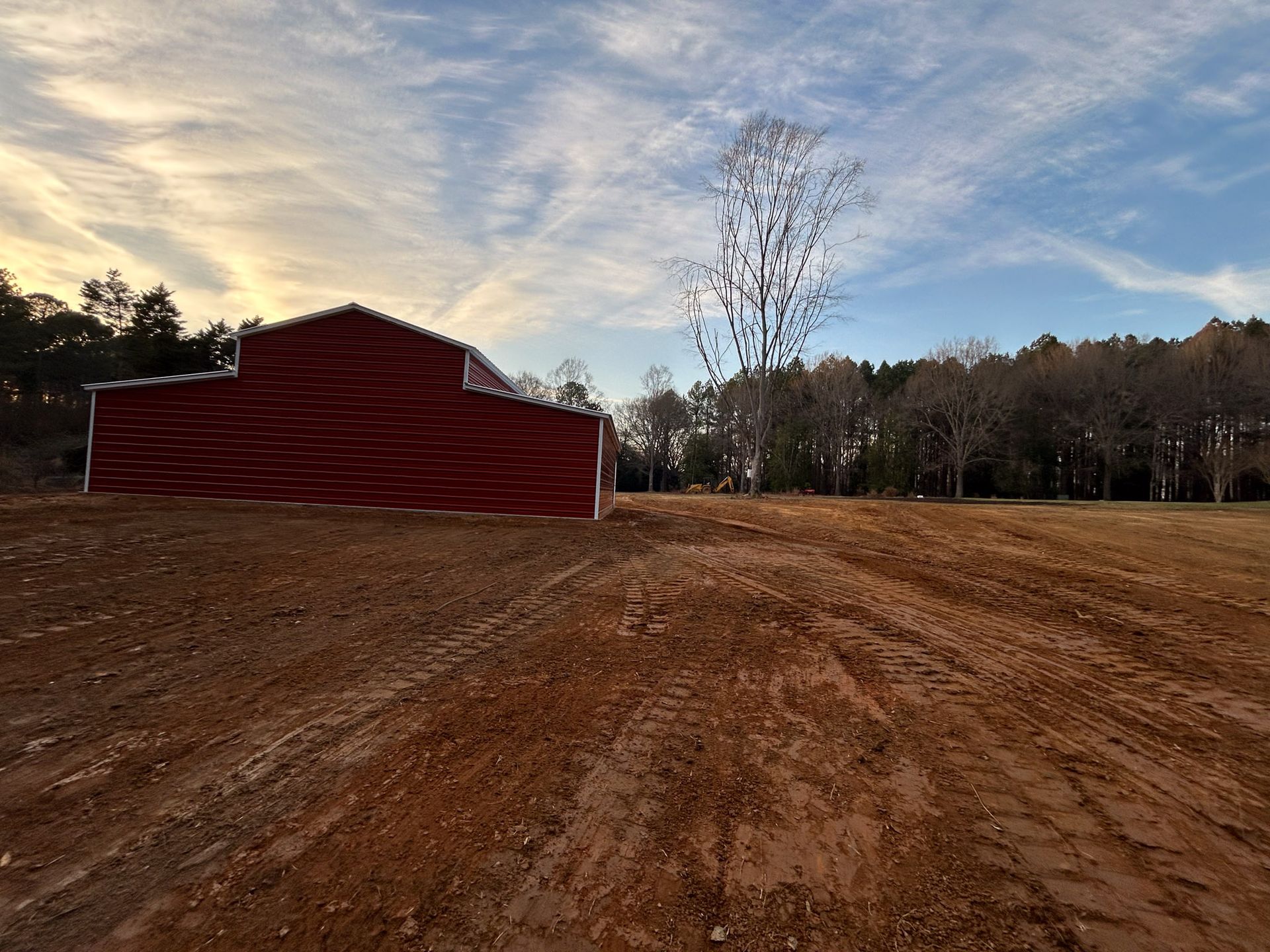 Red barn on brown dirt field under a cloudy sky.