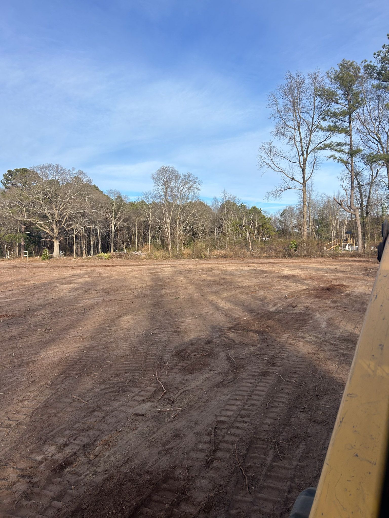 Cleared dirt lot with trees in the background under a blue sky.
