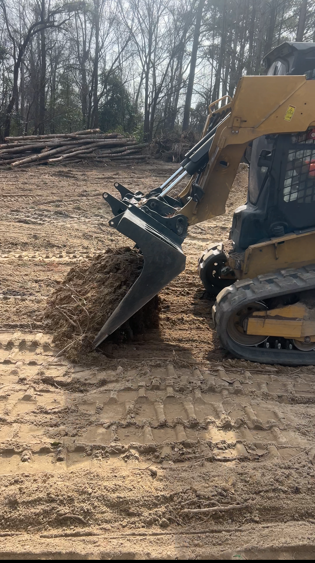 Skid steer with grapple digging into dirt in an outdoor setting.