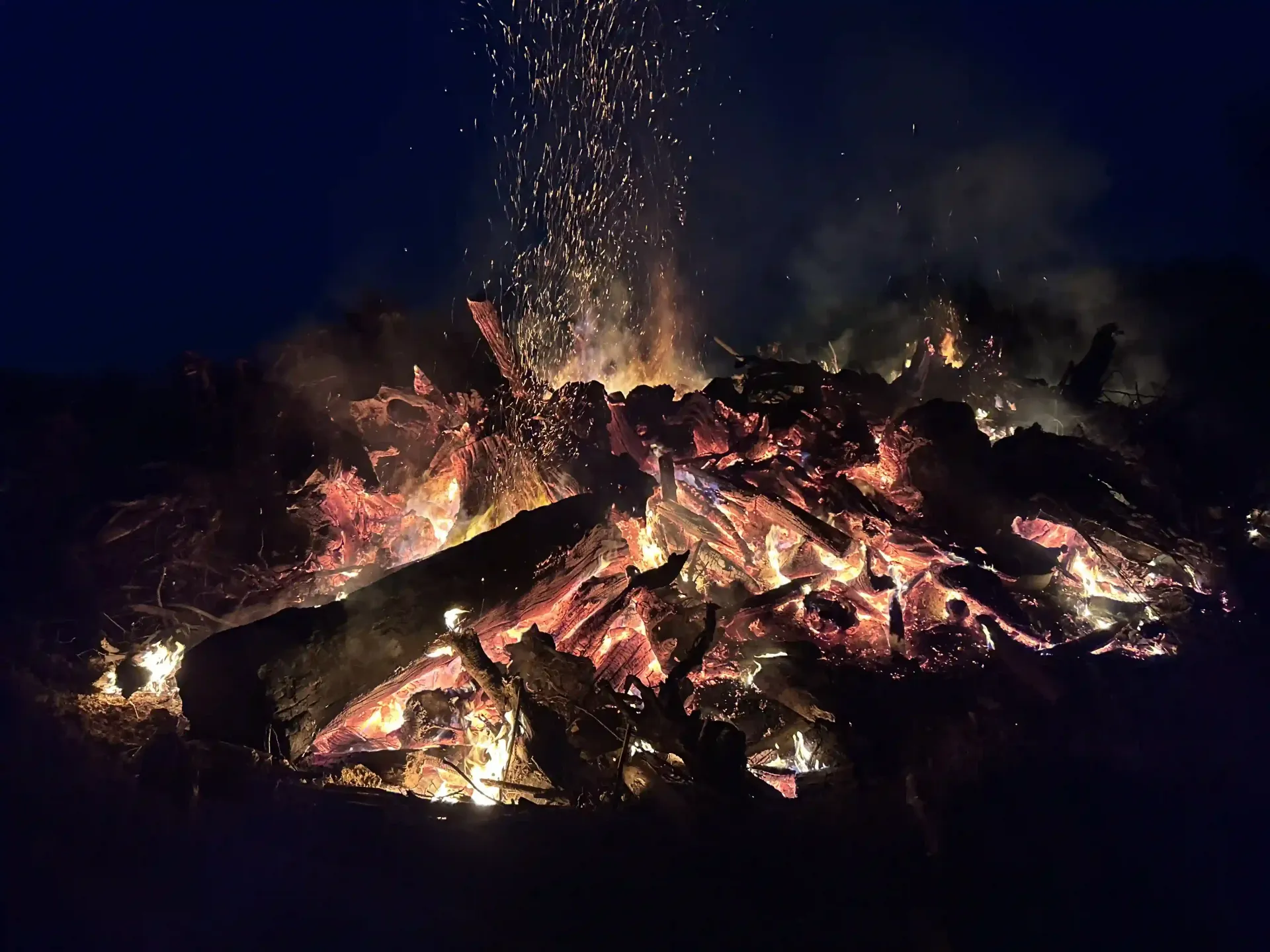 Glowing bonfire burning at night, with bright embers and sparks rising against a dark background