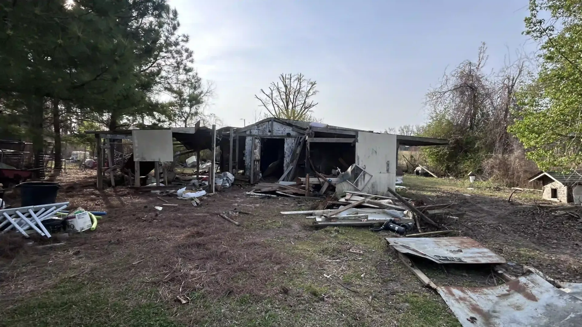 Burned-out house with damaged roof and debris scattered across the yard