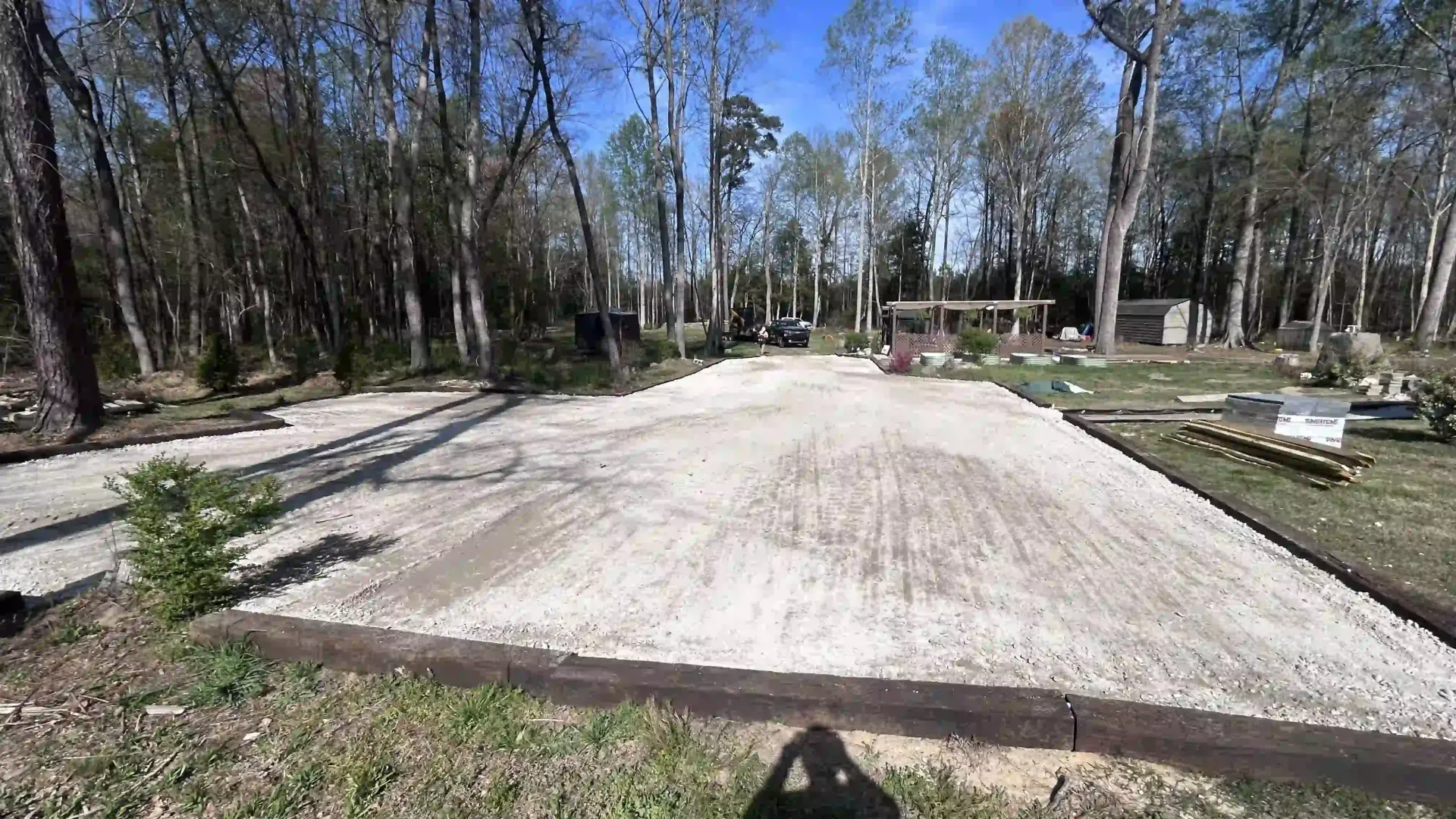 Empty concrete slab in a wooded park, with trees and picnic tables around it.