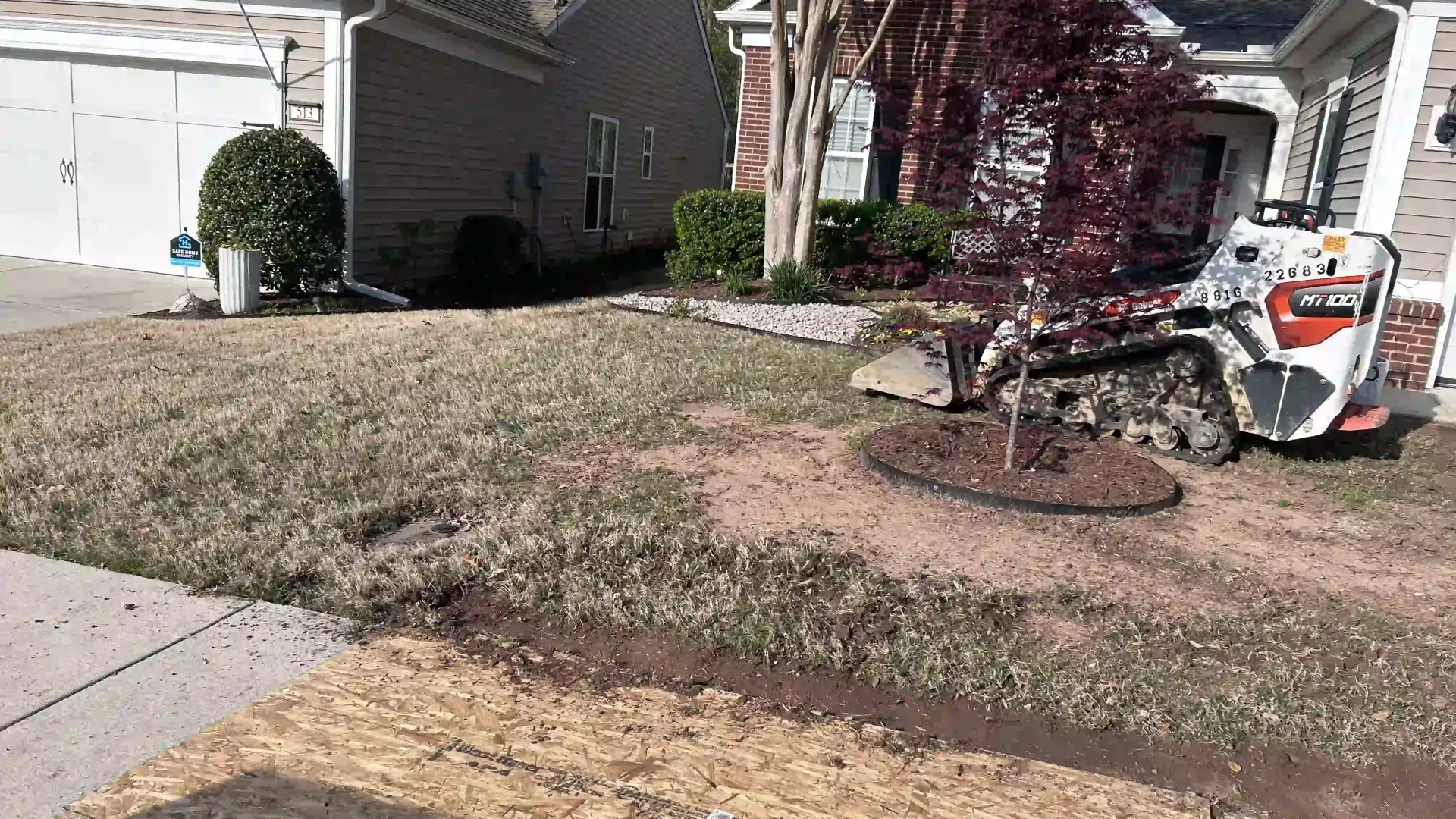 Residential front yard with a tree, walkway, and a white skid-steer parked near the house