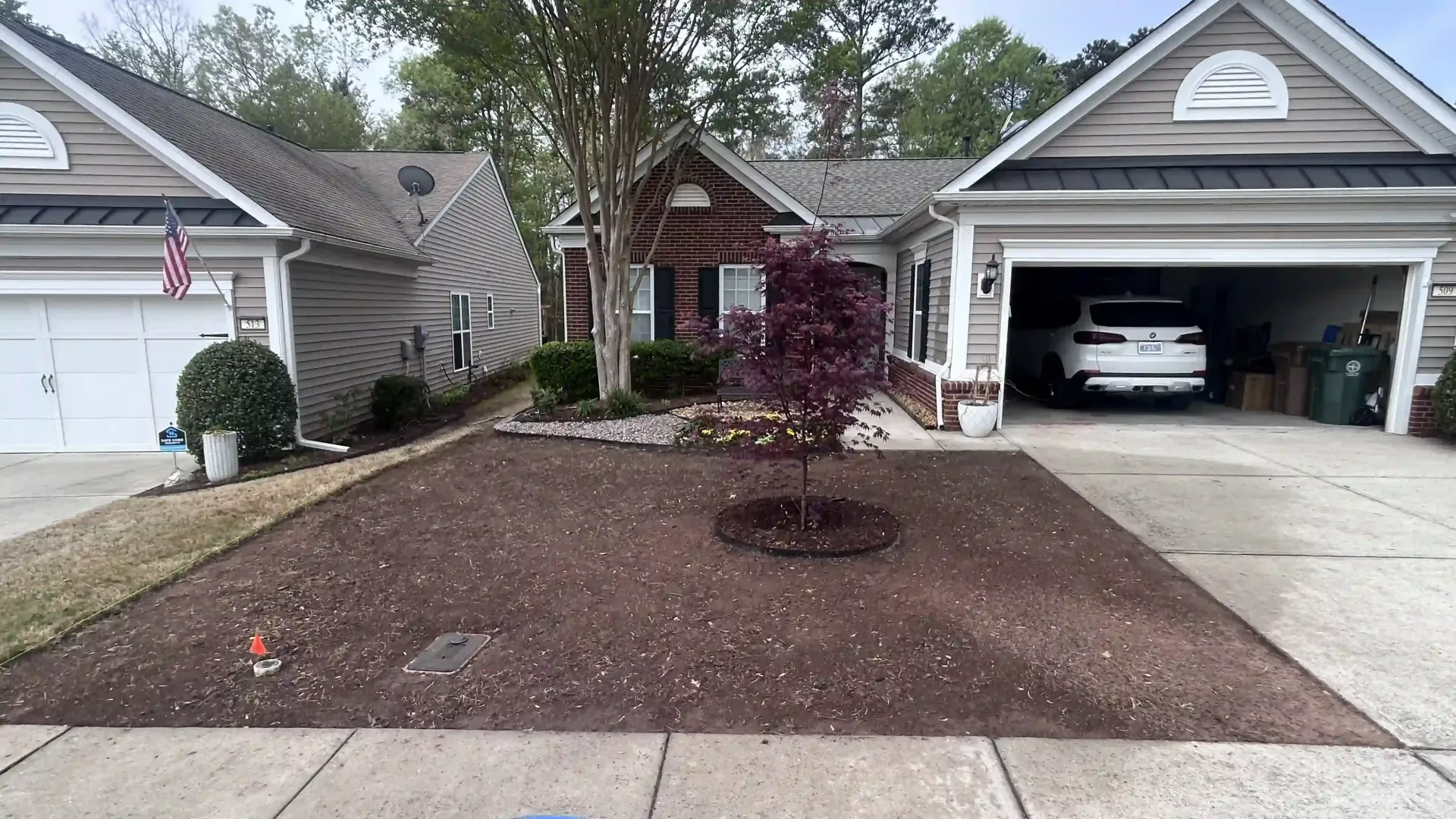 Suburban house with a mulched front yard, small tree, and open garage with a car inside
