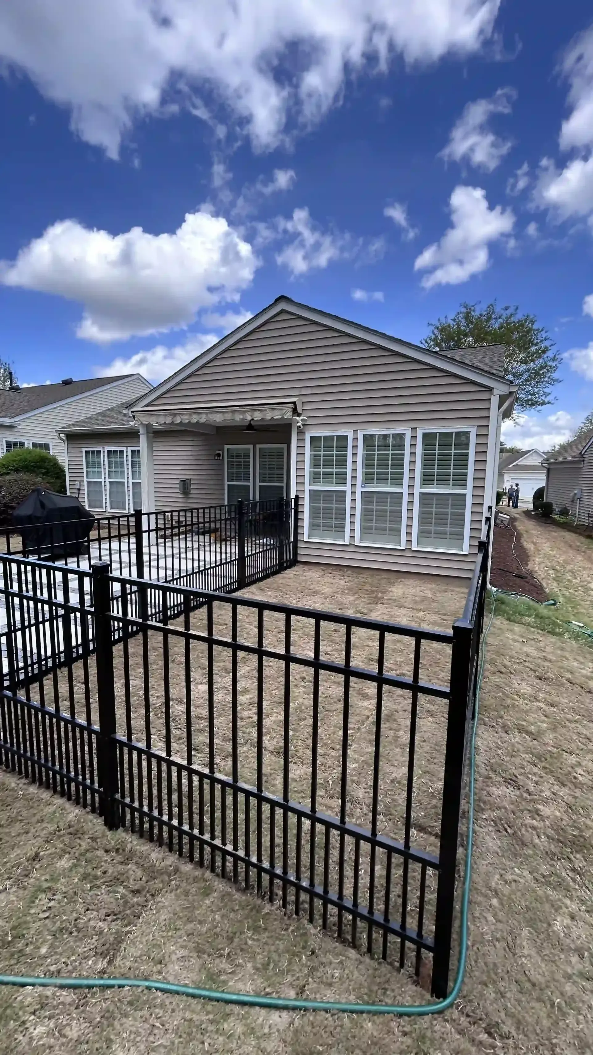 Black metal gate in front of a small screened porch and house under a blue sky with clouds