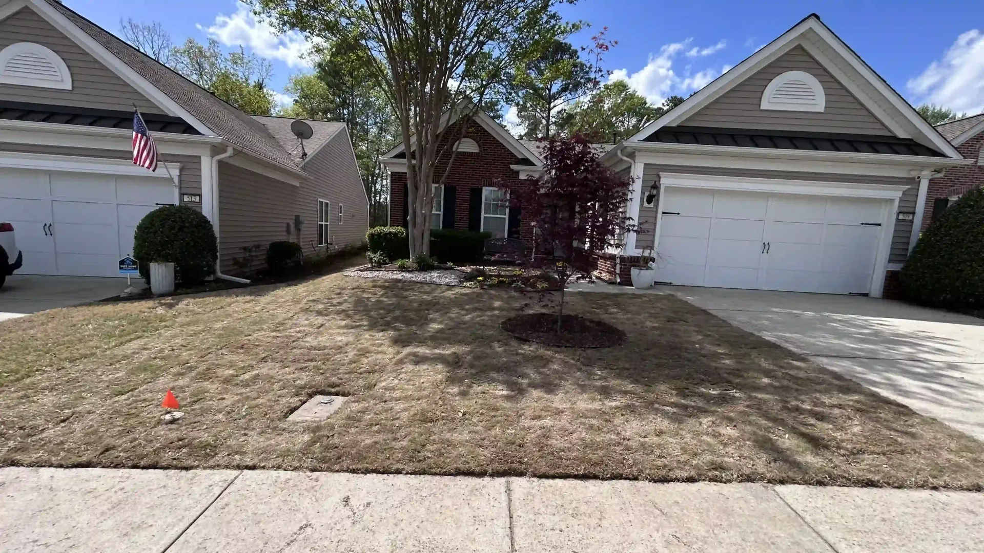 Suburban house front yard with dry grass, two garages, and a small tree in the center