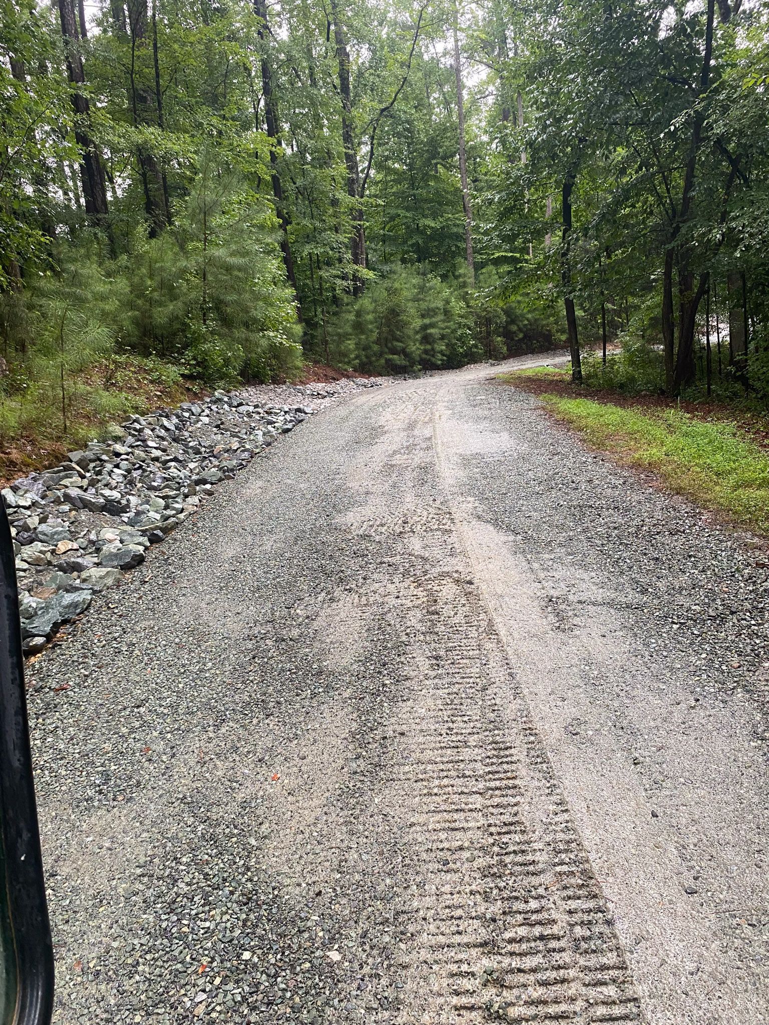 Gravel road winds through trees. Tire tracks run down center, rocks line edges.