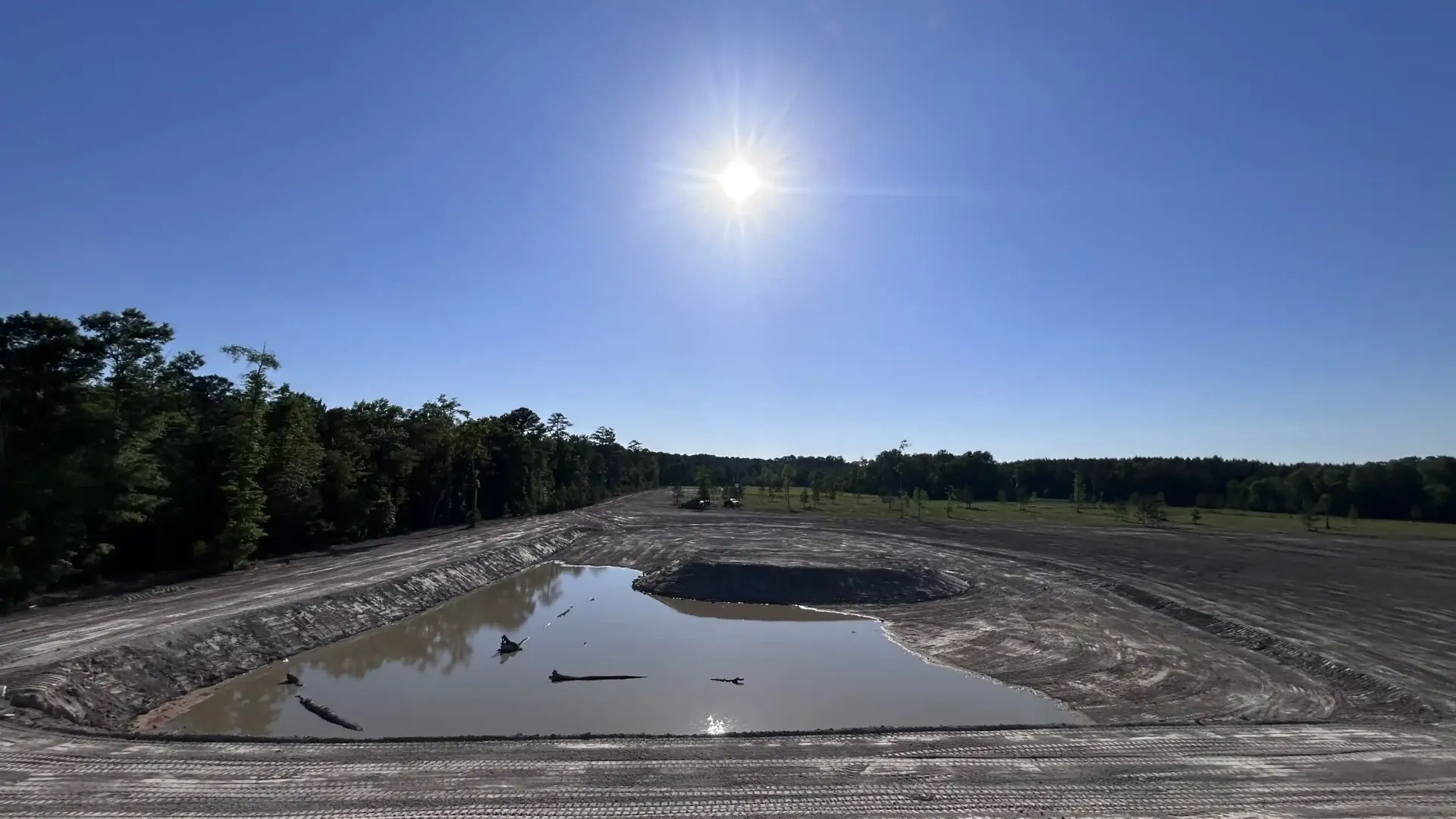 Sunny rocky quarry with a small puddle and tree-lined horizon under a clear blue sky