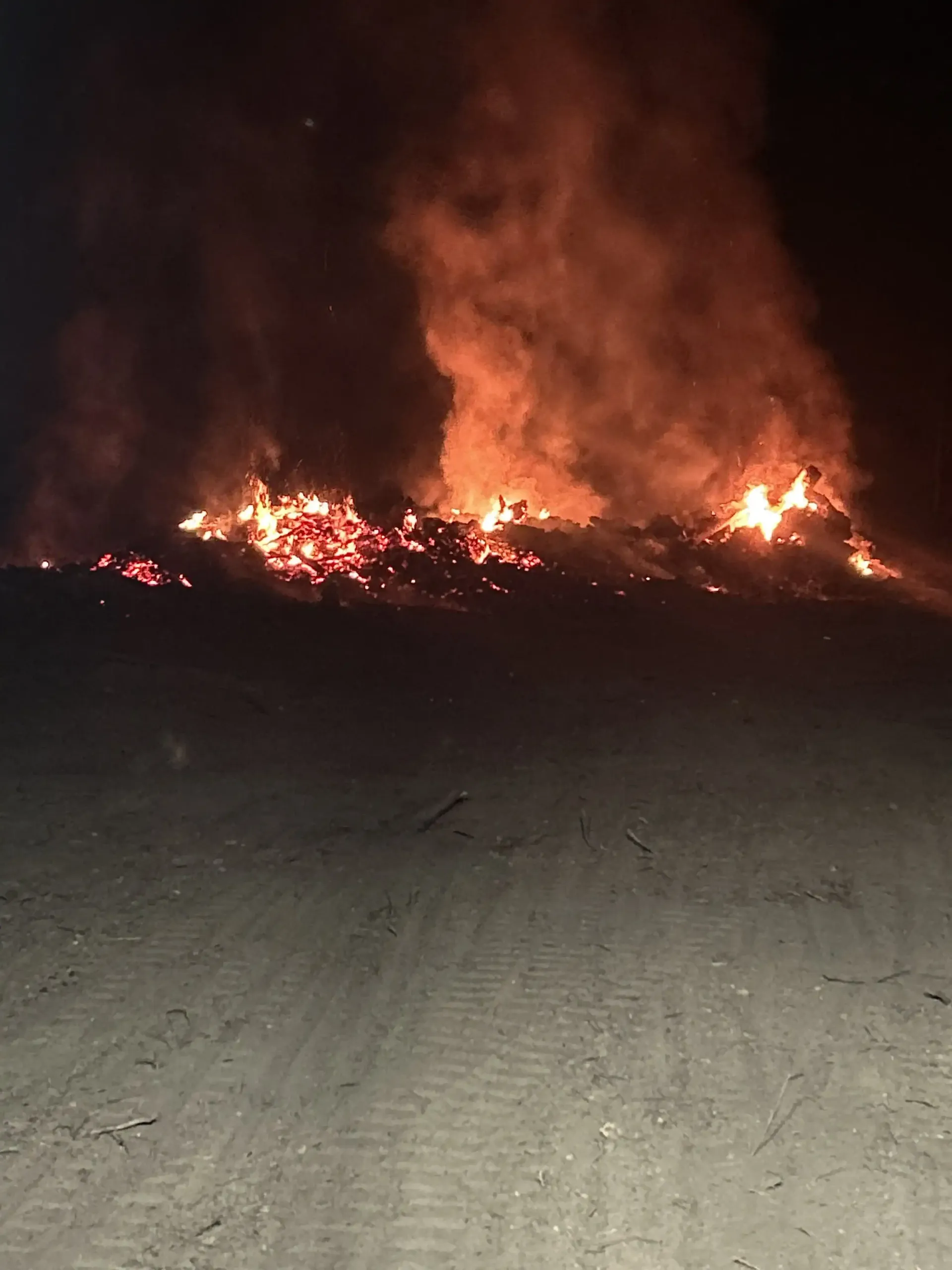 Nighttime wildfire blazing across a field, with flames and smoke on the horizon