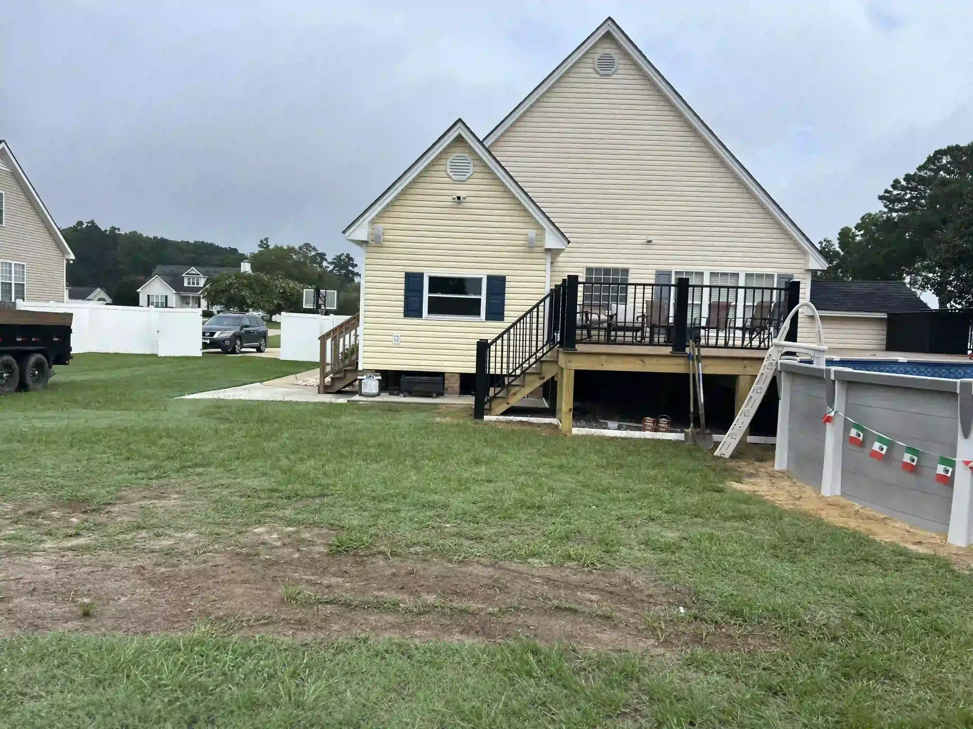 A beige house with a raised deck and stairs, viewed from a grassy backyard with a cloudy sky.