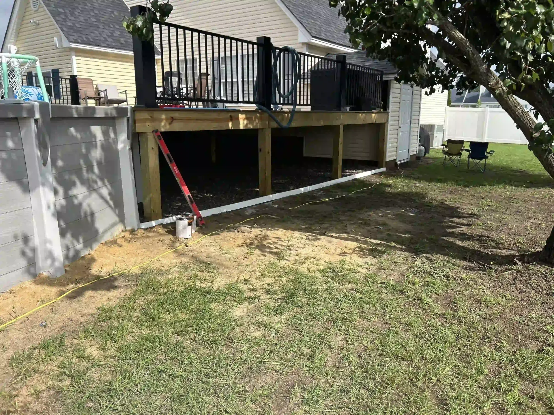 Backyard with raised wooden deck, black railing, patio posts, and a red ladder leaning underneath.