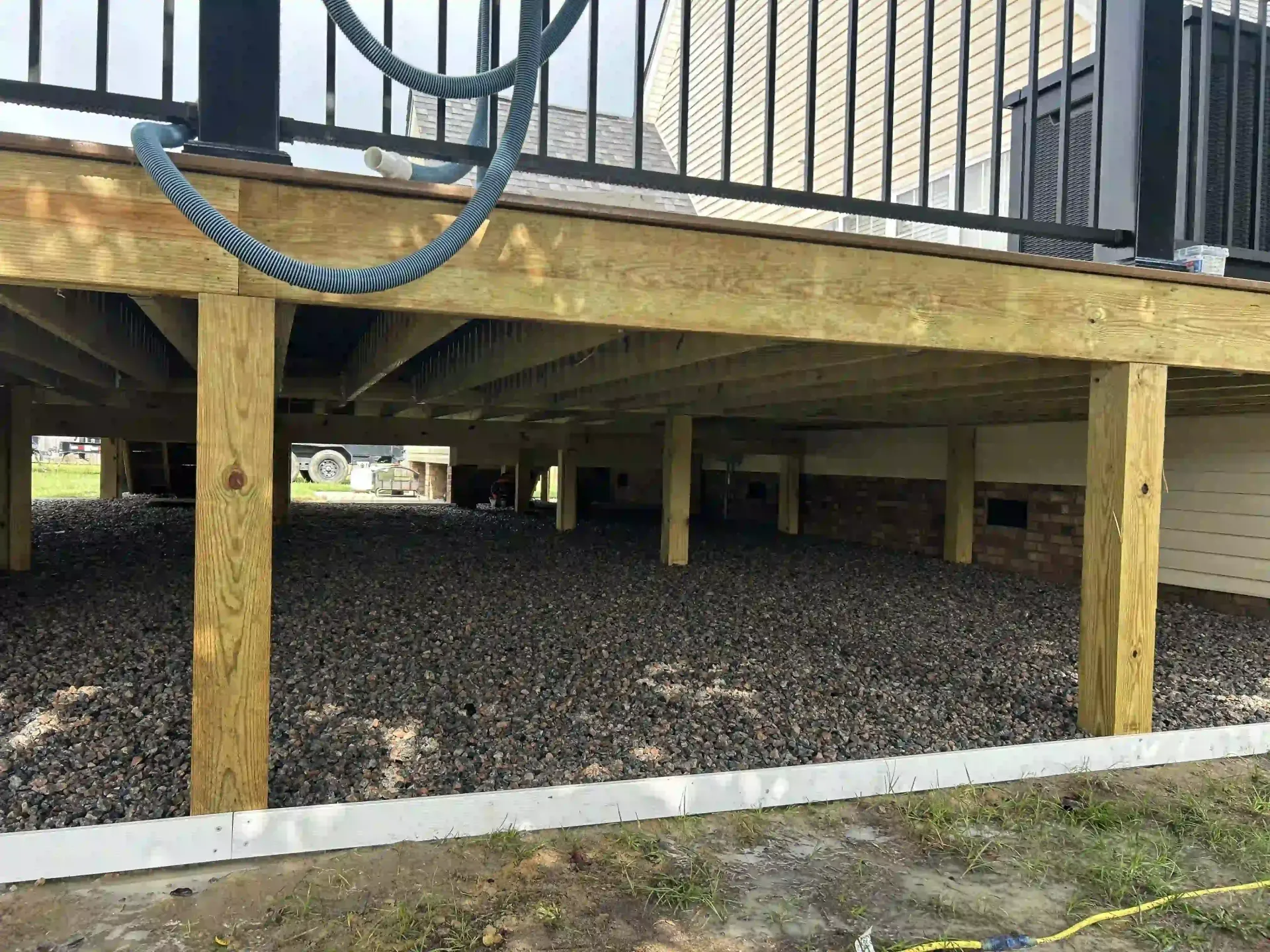 Raised wooden deck with black railings and rope swing over a gravel-covered area outdoors