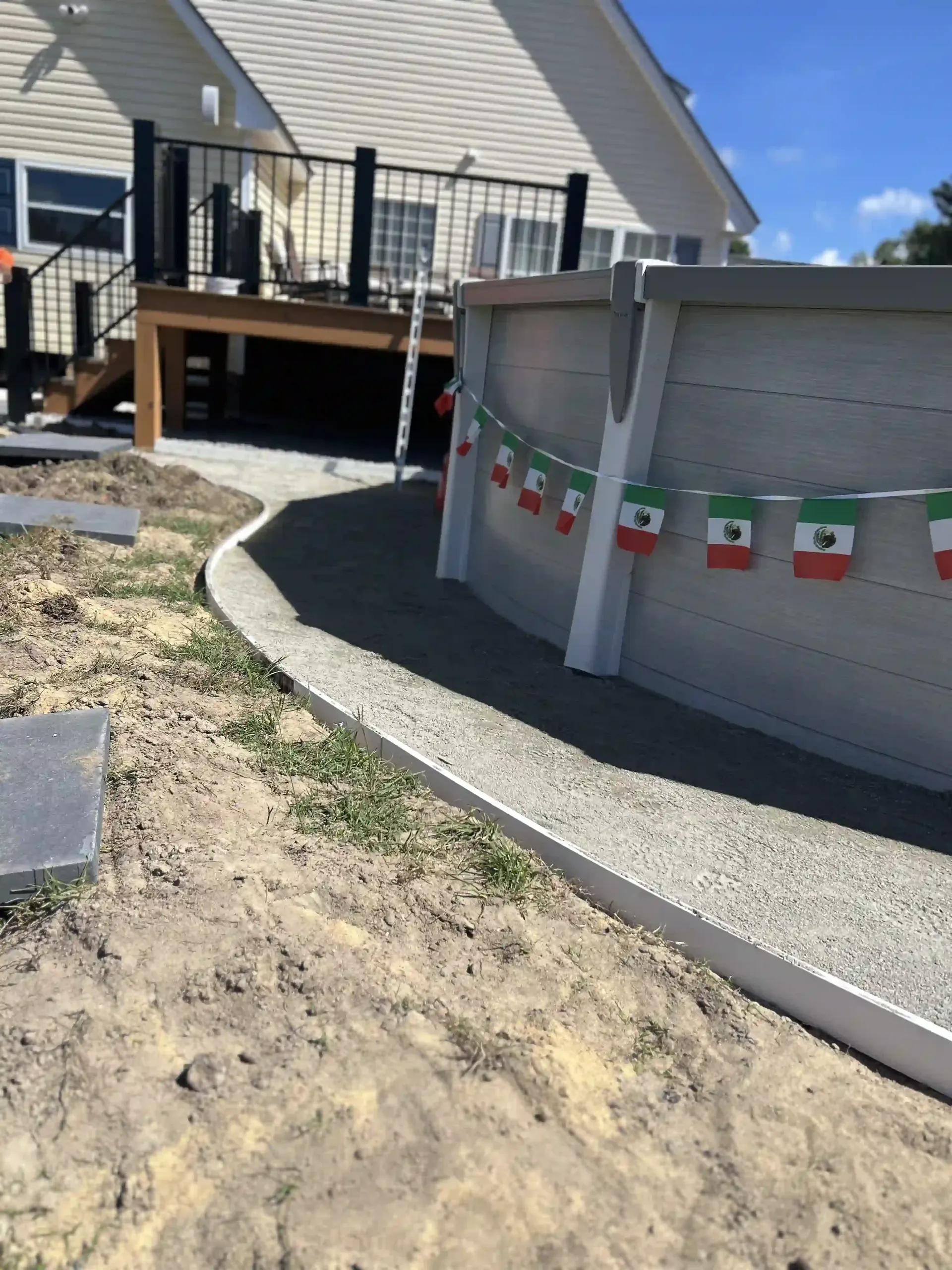 Backyard deck and gray retaining wall with festive hanging decorations, next to a gravel path.
