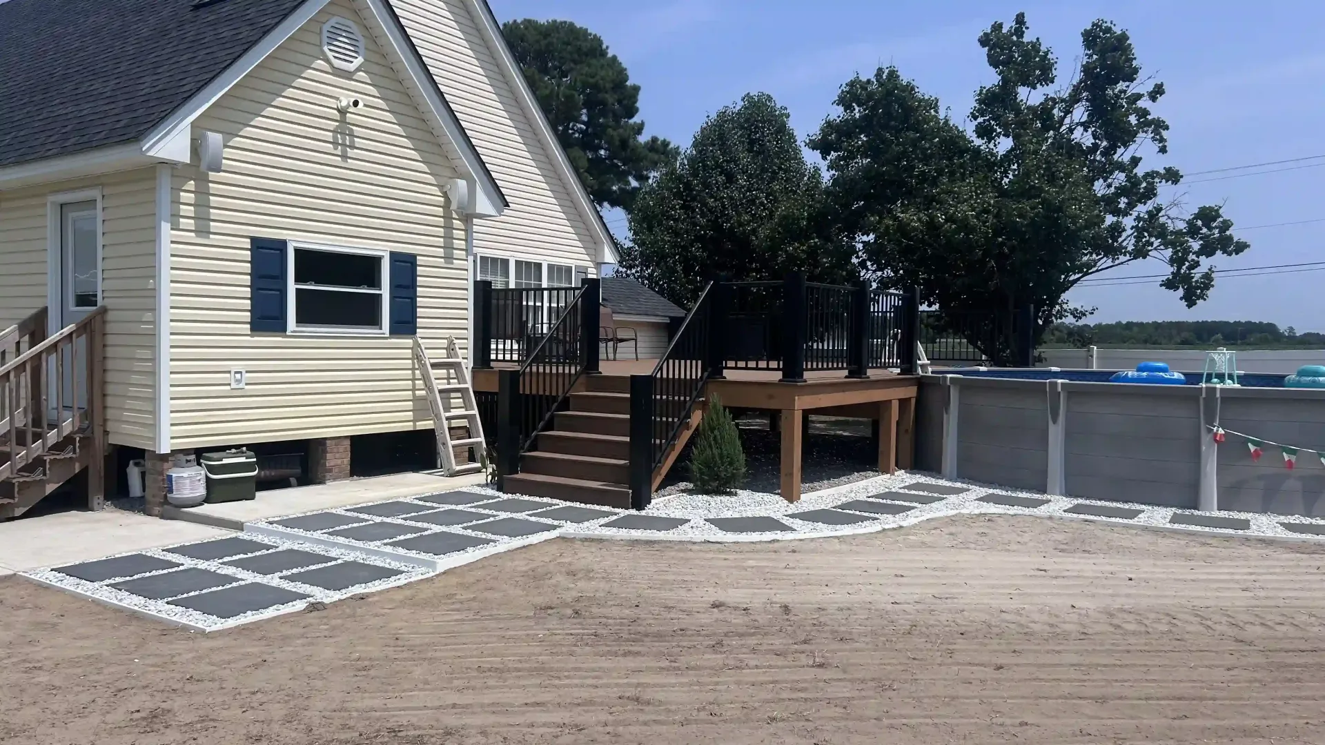 House with raised wooden deck and steps beside a fenced sandy yard near the water
