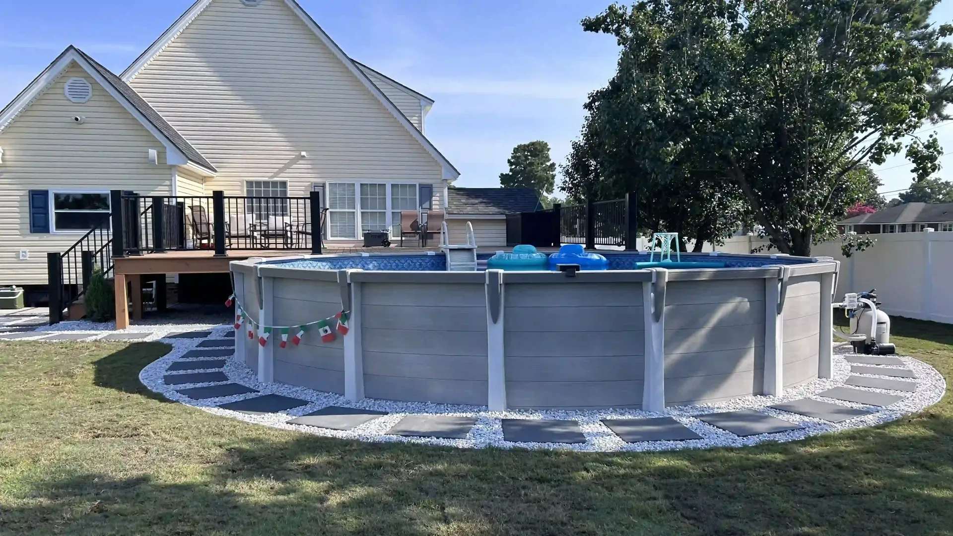 Backyard above-ground pool with blue water beside a beige house on a sunny day