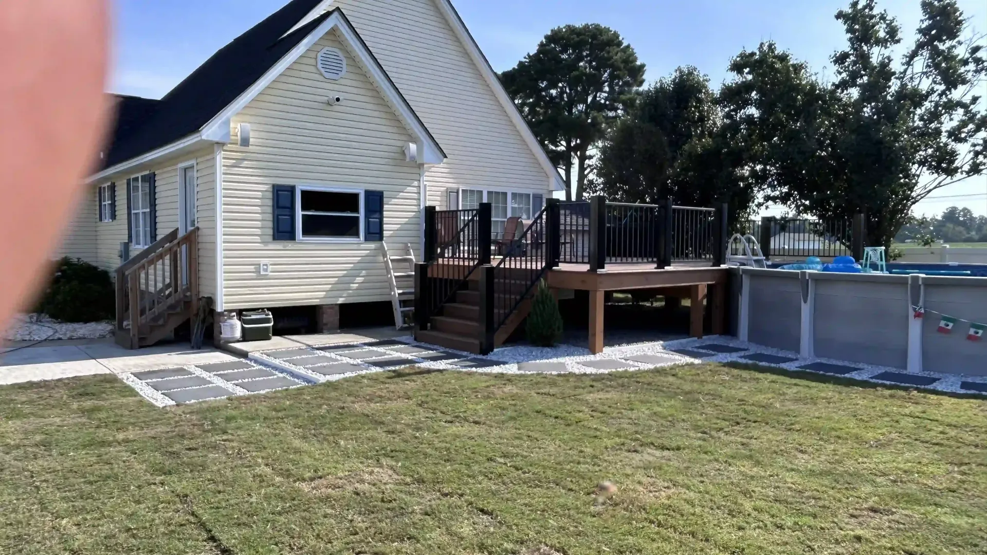 White house with blue shutters, wooden deck, and above-ground pool in a sunny yard
